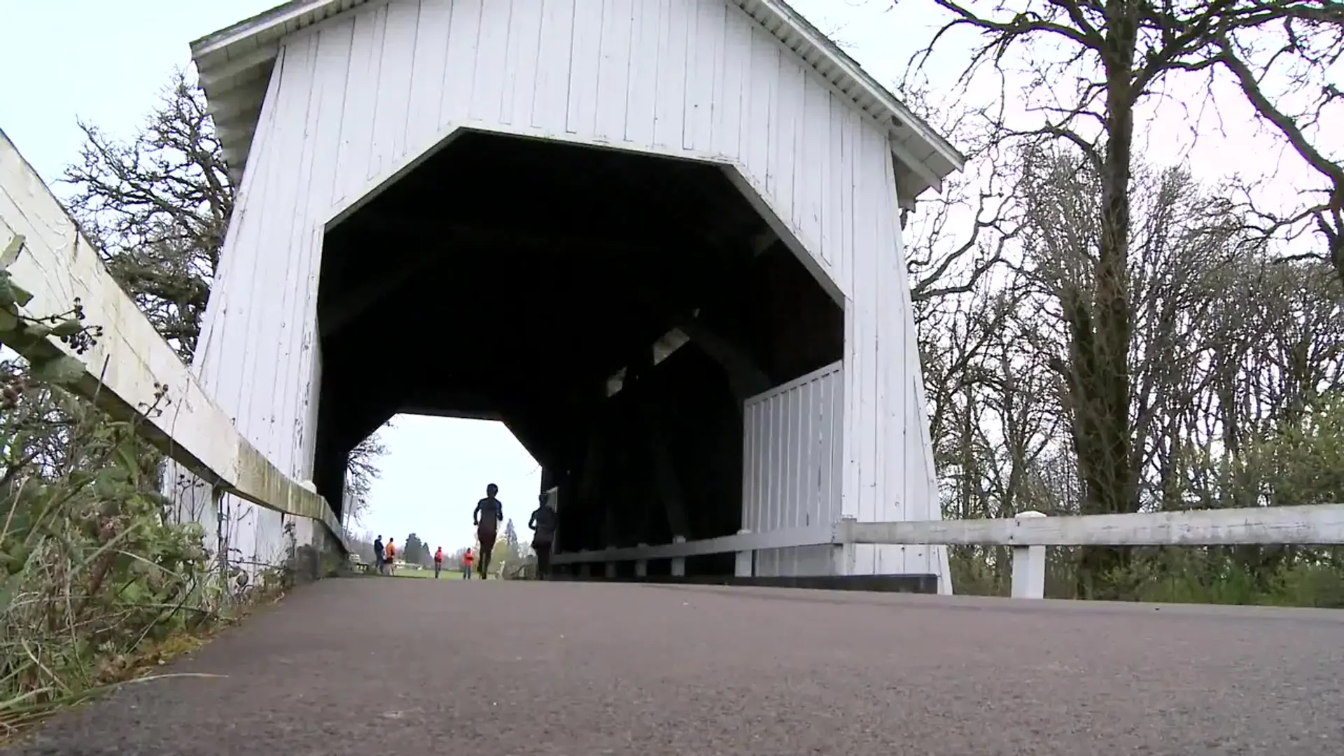 The image shows a traditional covered bridge with a white exterior. There is a roadway