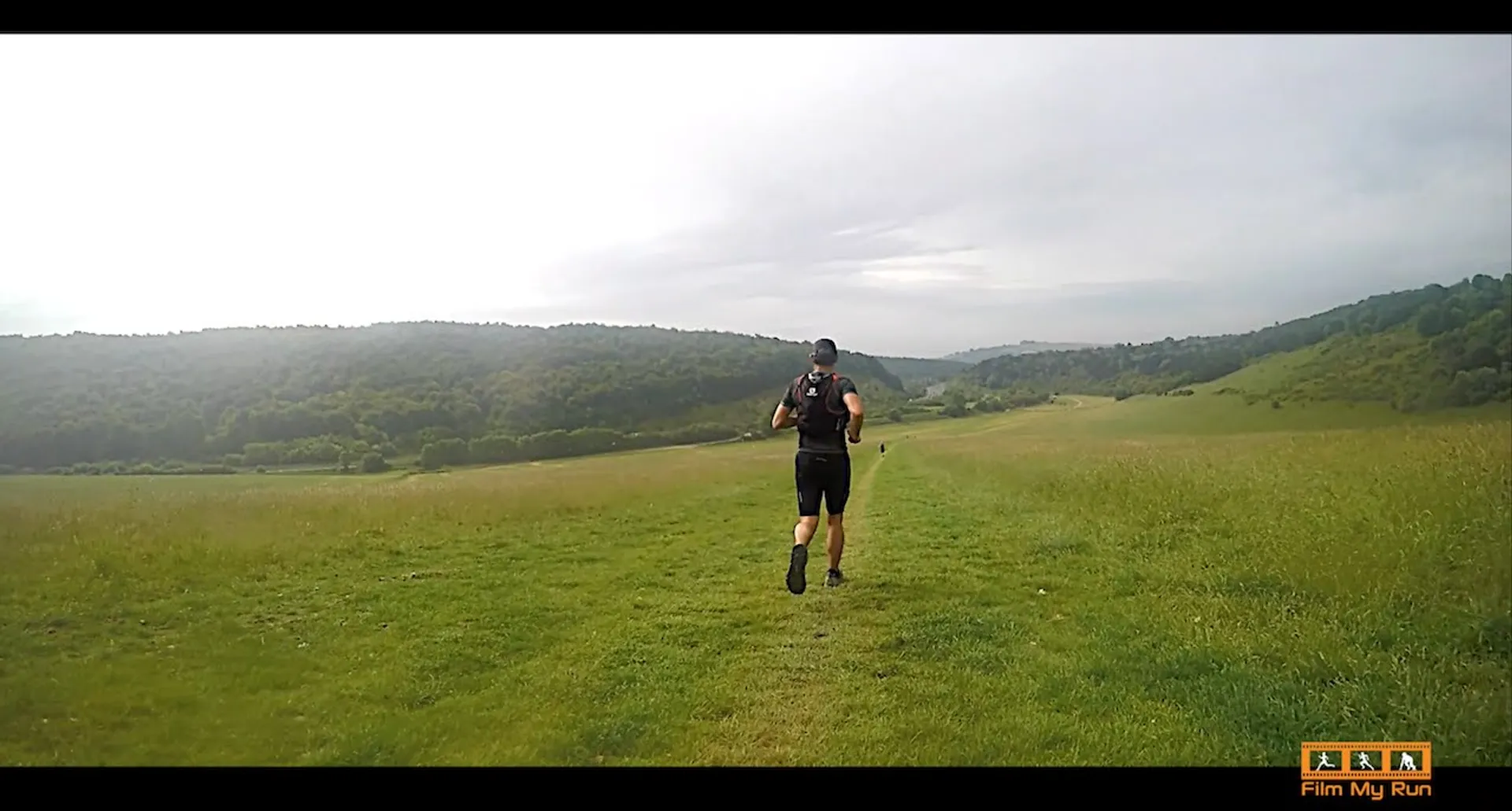 The image shows an individual running through a grassy field or meadow. The