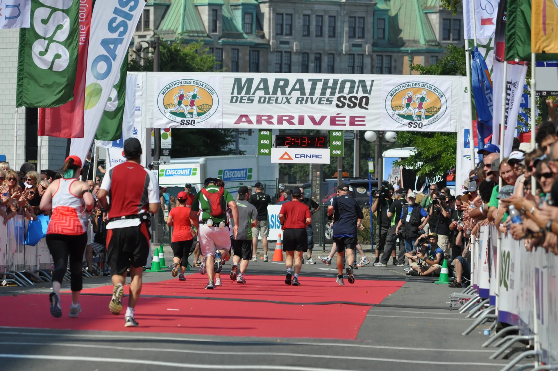 The image depicts a marathon event. Runners are crossing the finish line where a