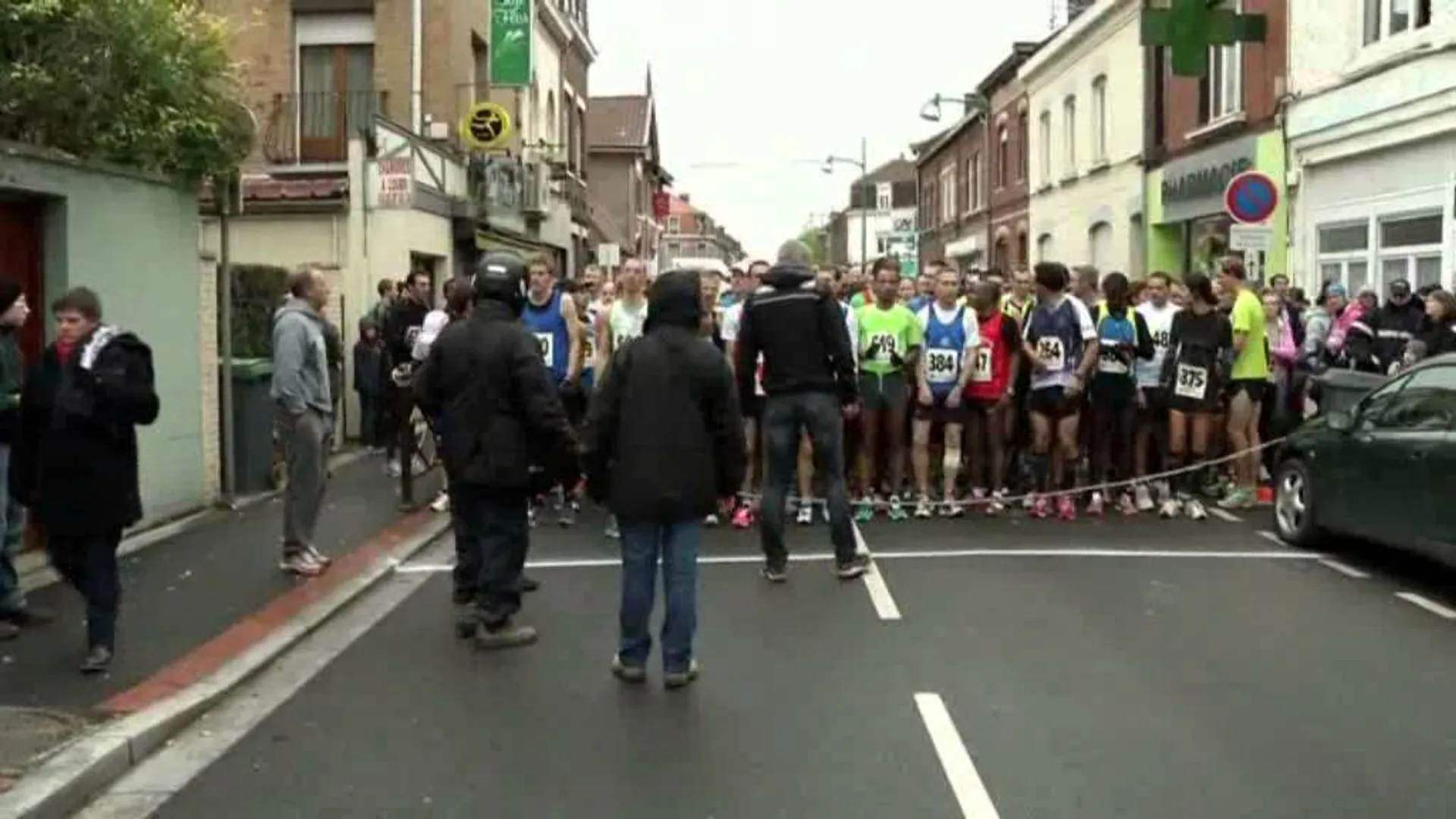 The image shows a group of runners lined up at the start line of a road