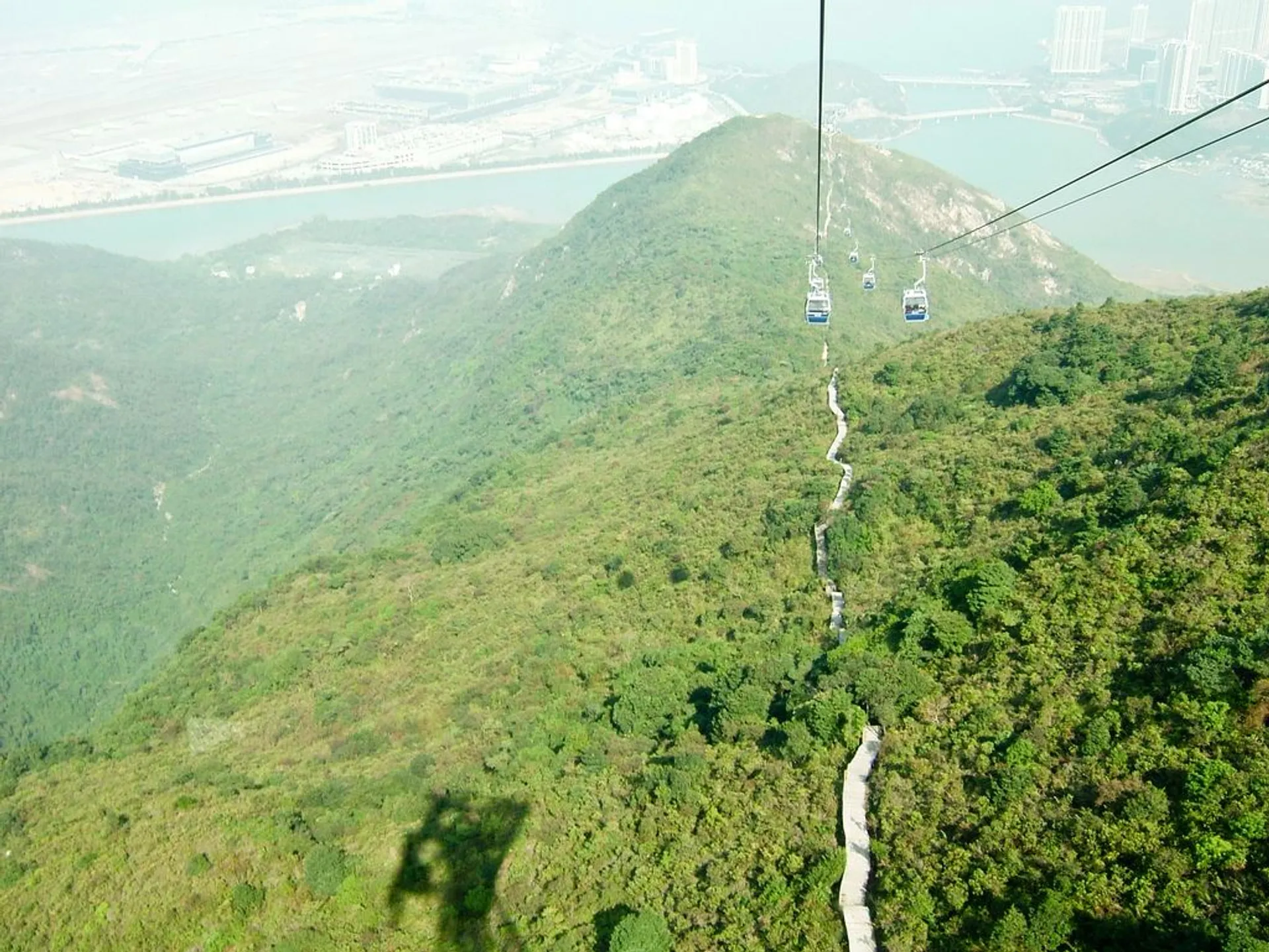 The image shows a cable car system with several cable cars traveling over a lush green
