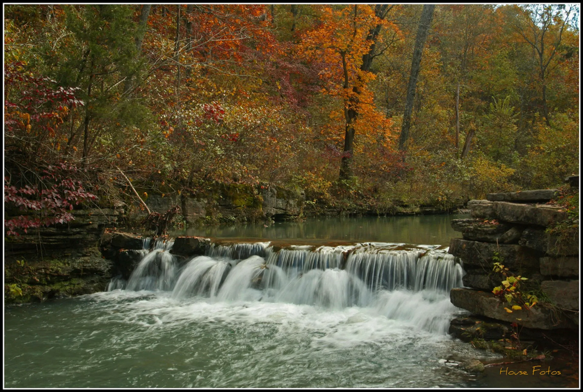 The image shows a serene natural scene with a small waterfall cascading over a rock