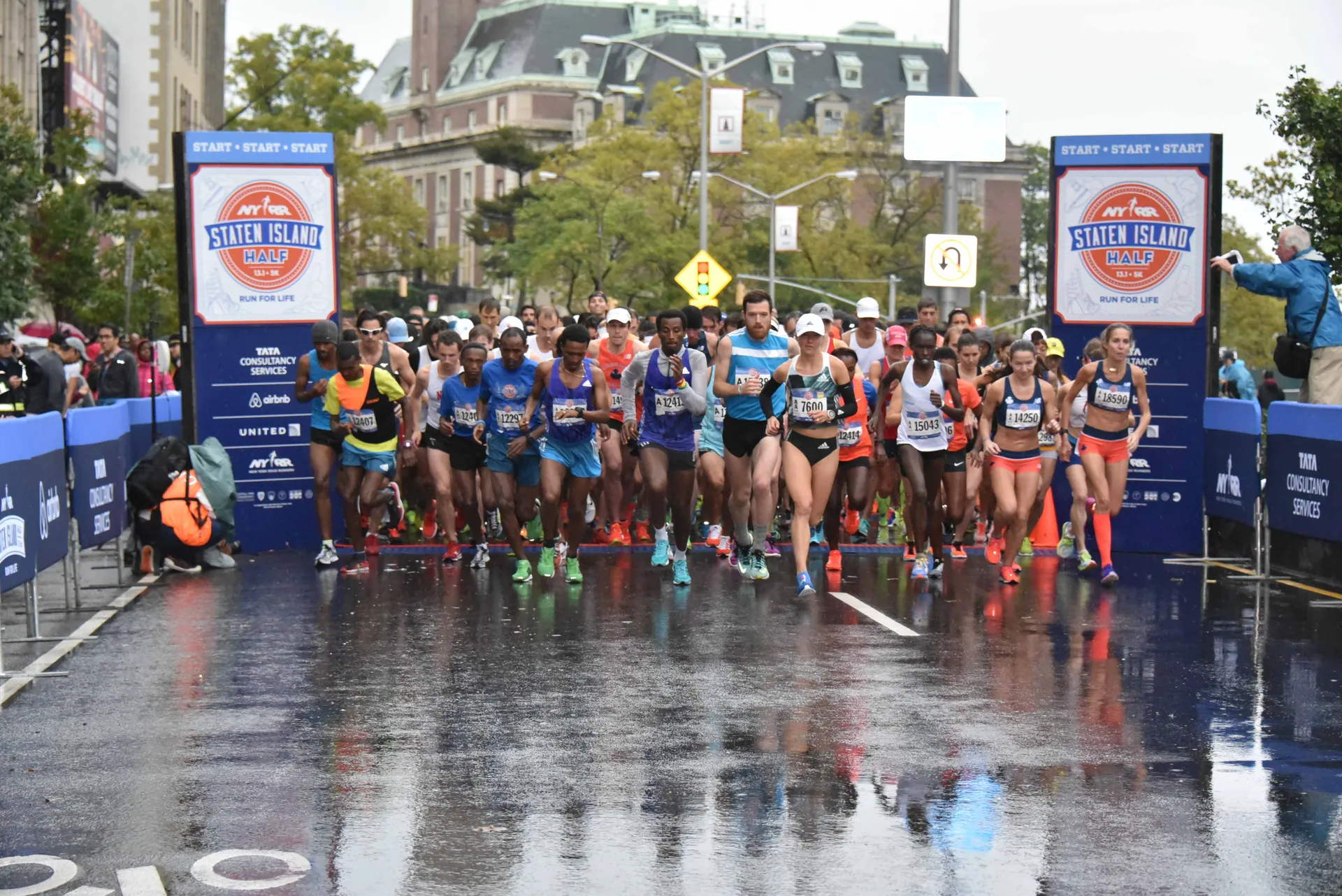 The image depicts a large group of runners at the start line of a marathon or