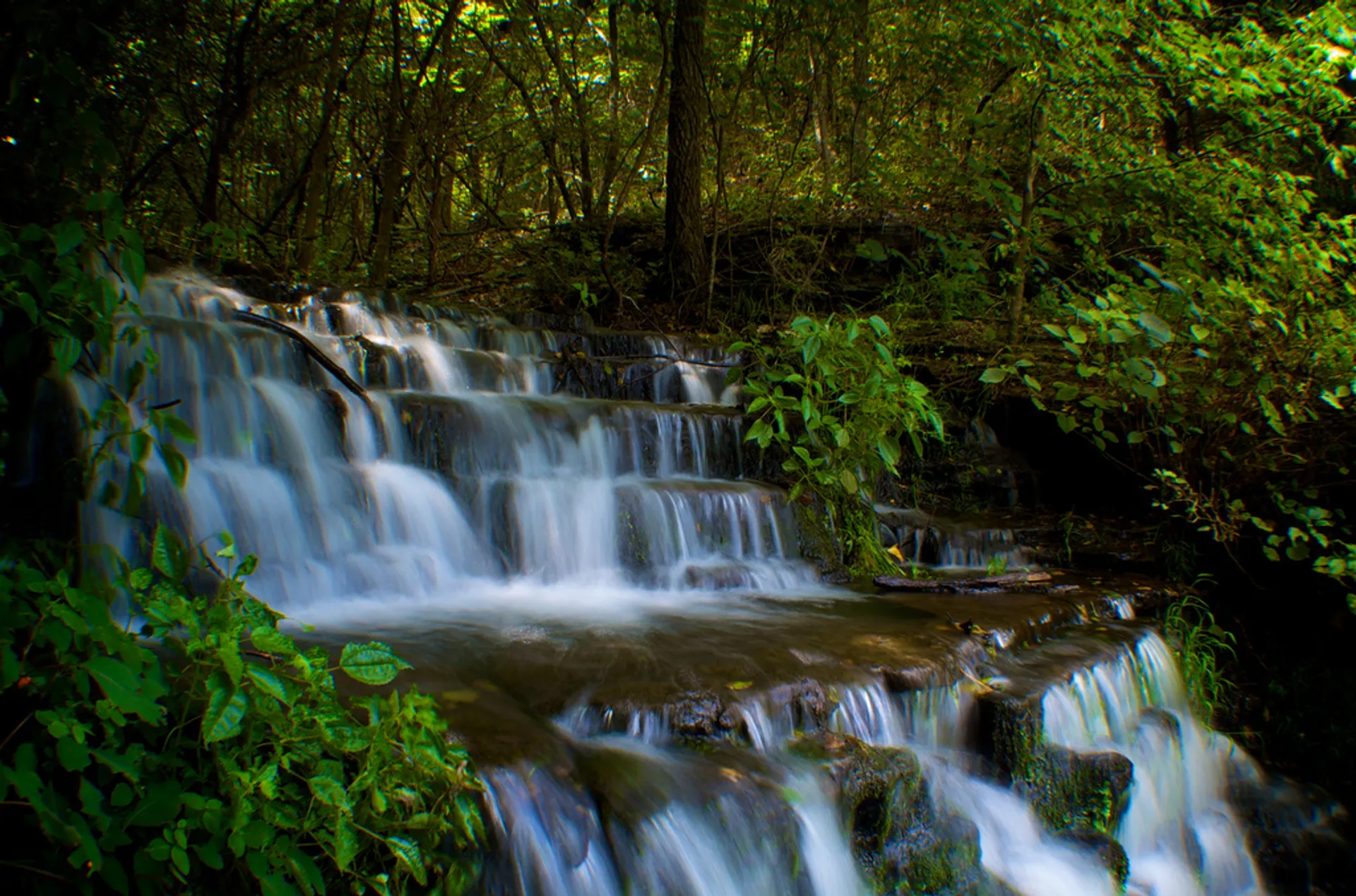 The image shows a beautiful, cascading waterfall in a wooded area. The water