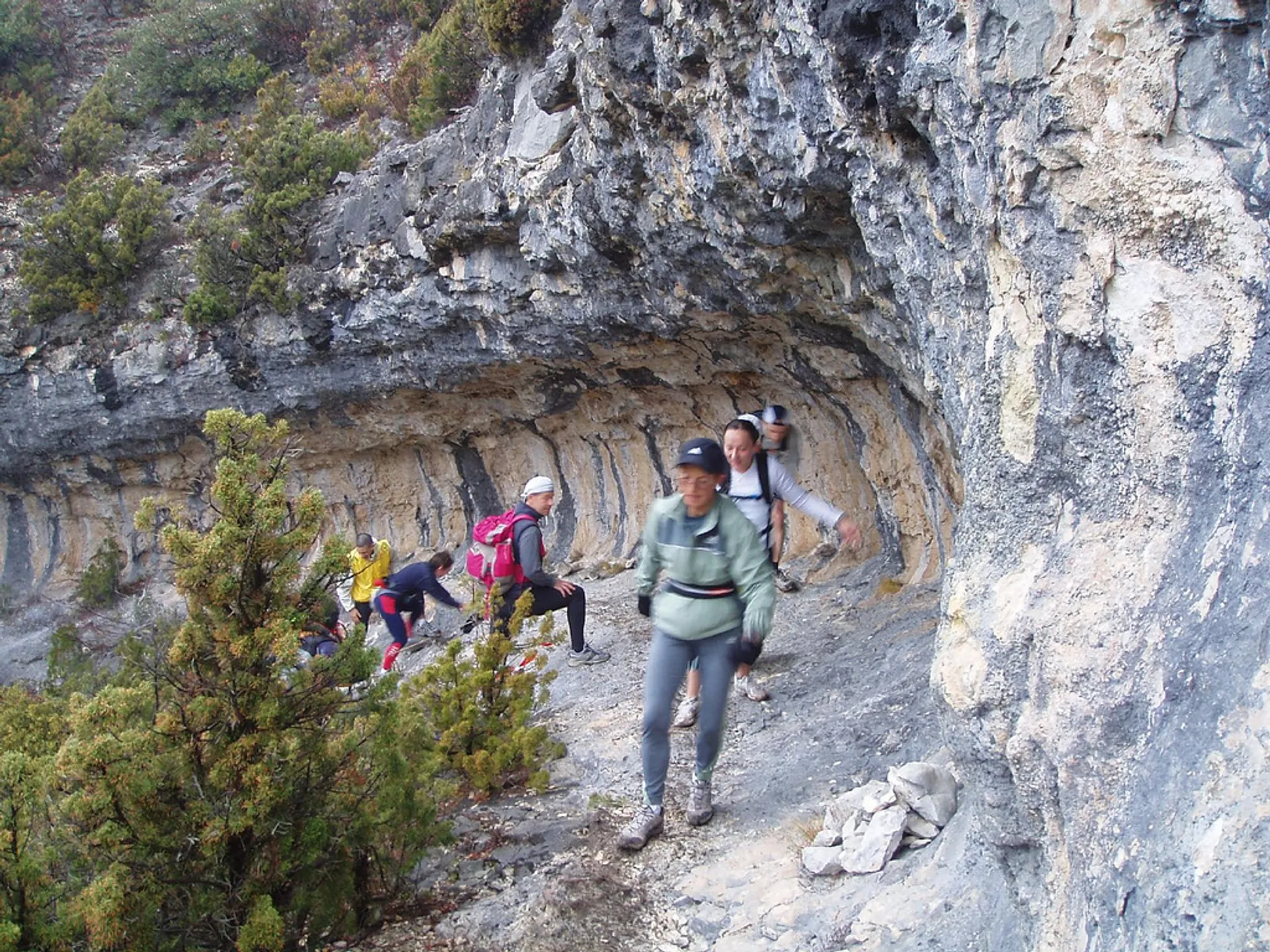 The image depicts a group of hikers navigating through a rocky mountain trail. The