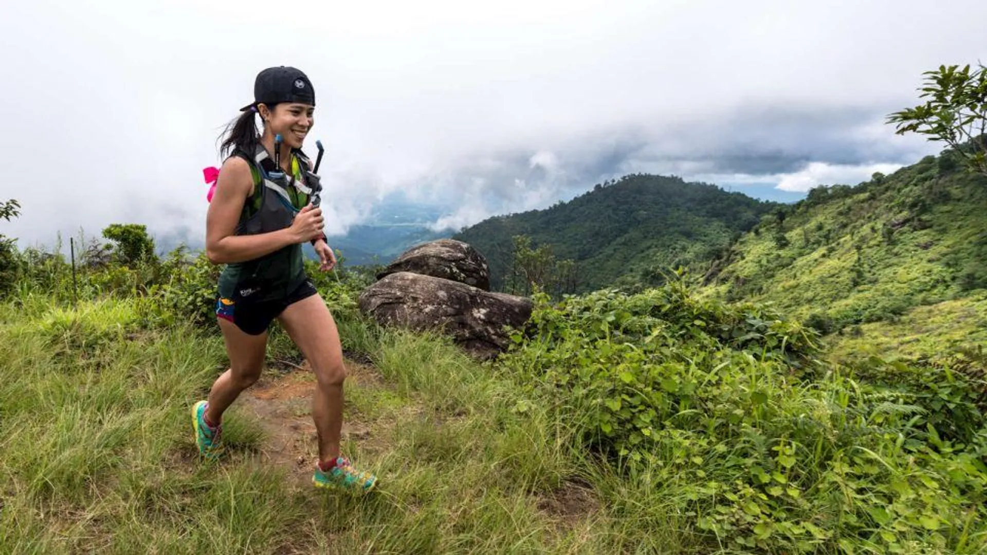 The image shows a person trail running through a beautiful, lush landscape. The runner
