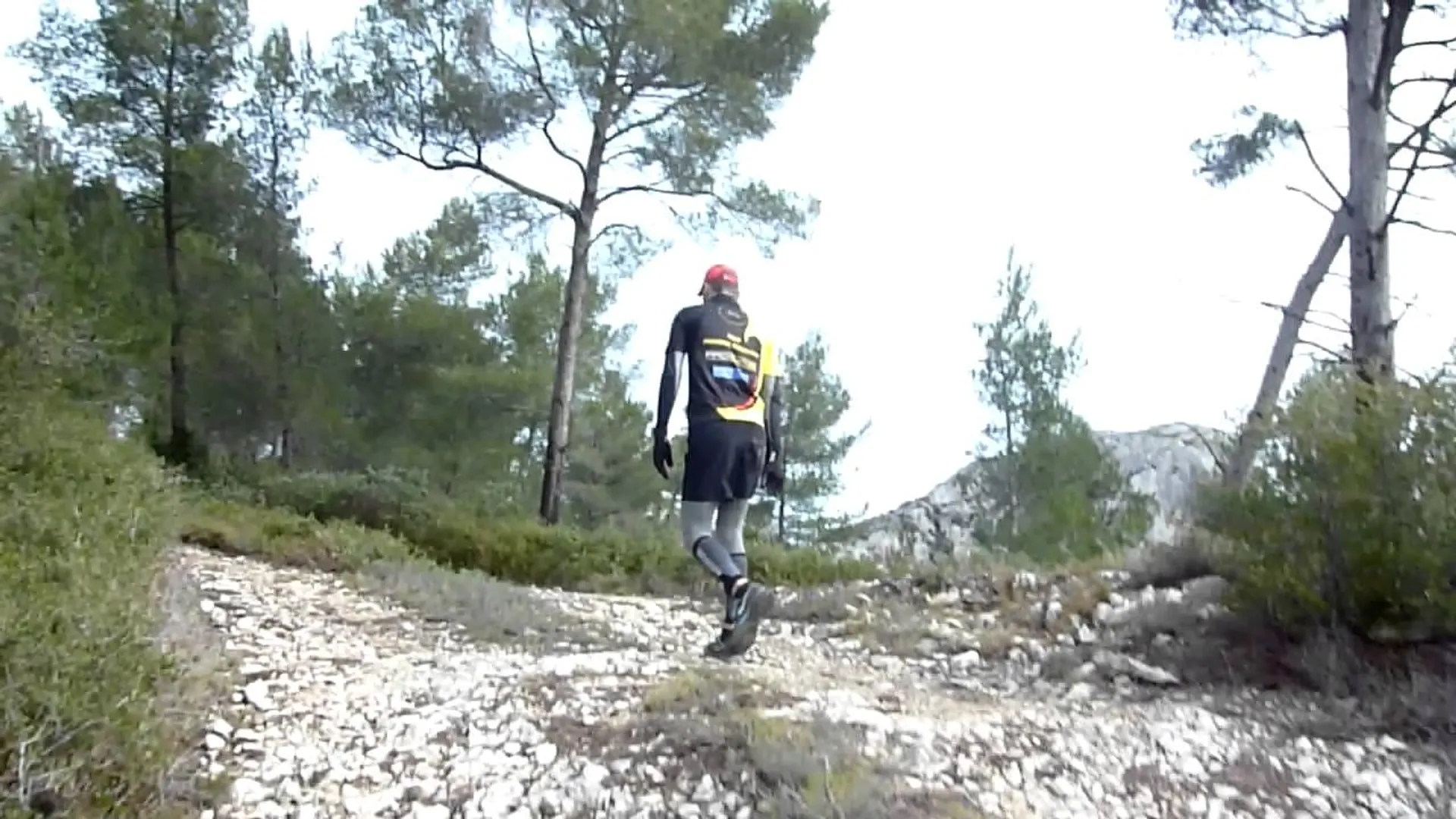 The image shows an individual walking on a rocky trail in a natural setting that appears
