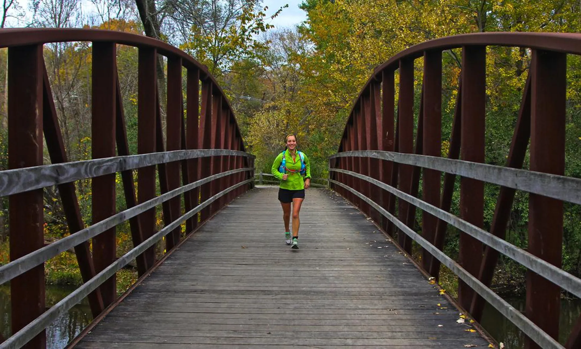 The image shows a person jogging towards the camera on a wooden footbridge. The