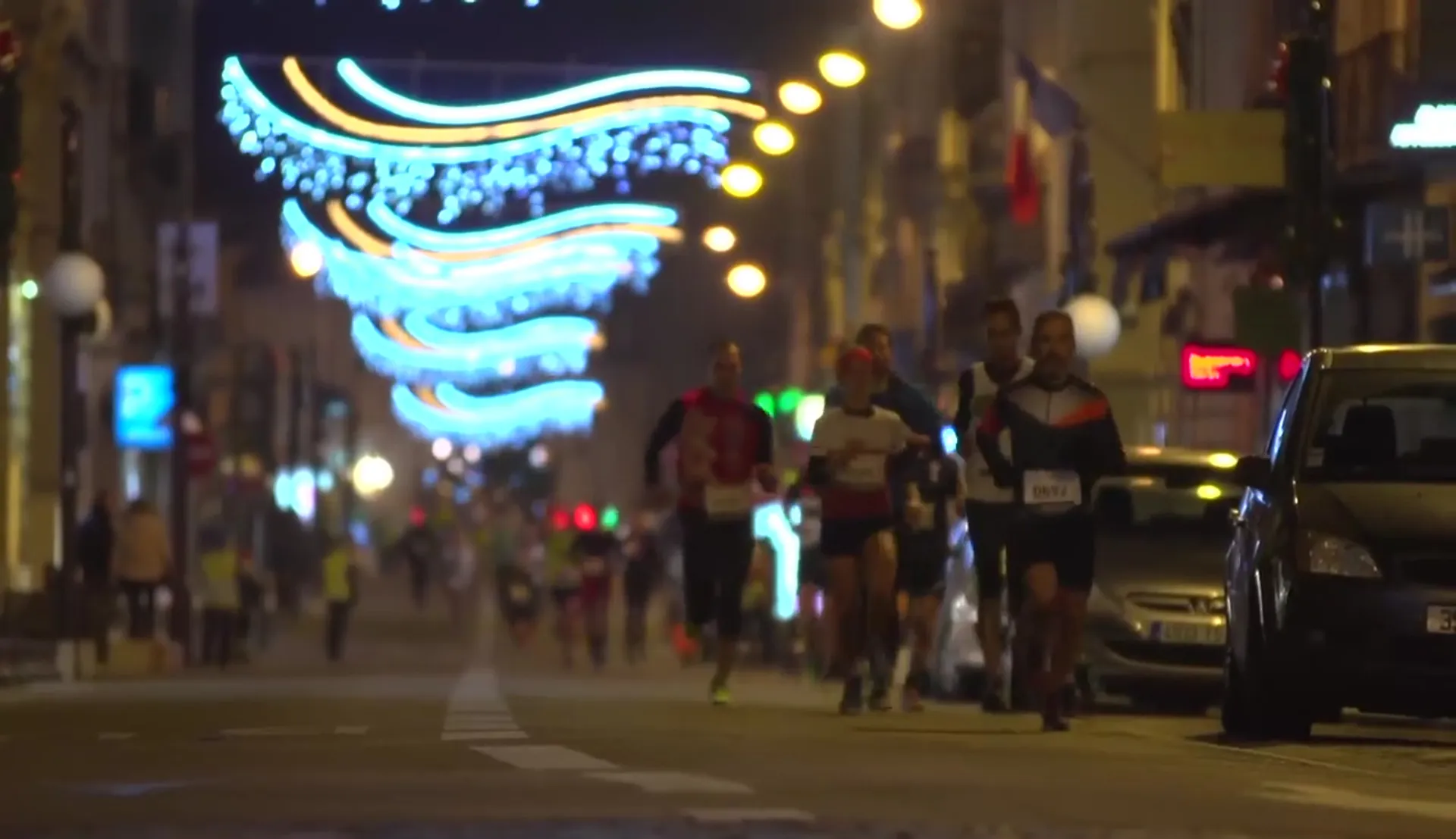 The image shows a nighttime street scene with a group of runners participating in what appears