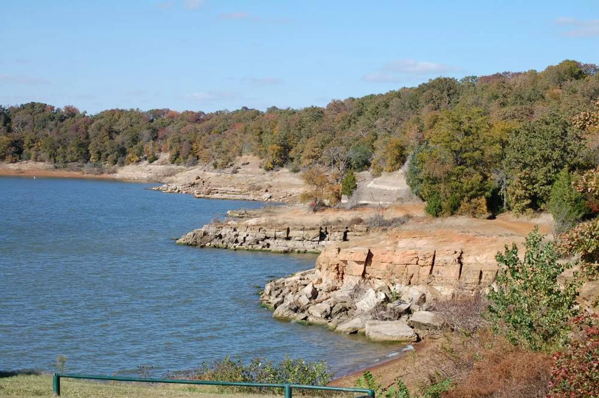 The image depicts a tranquil lake with a rocky shoreline surrounded by trees displaying autumn colors