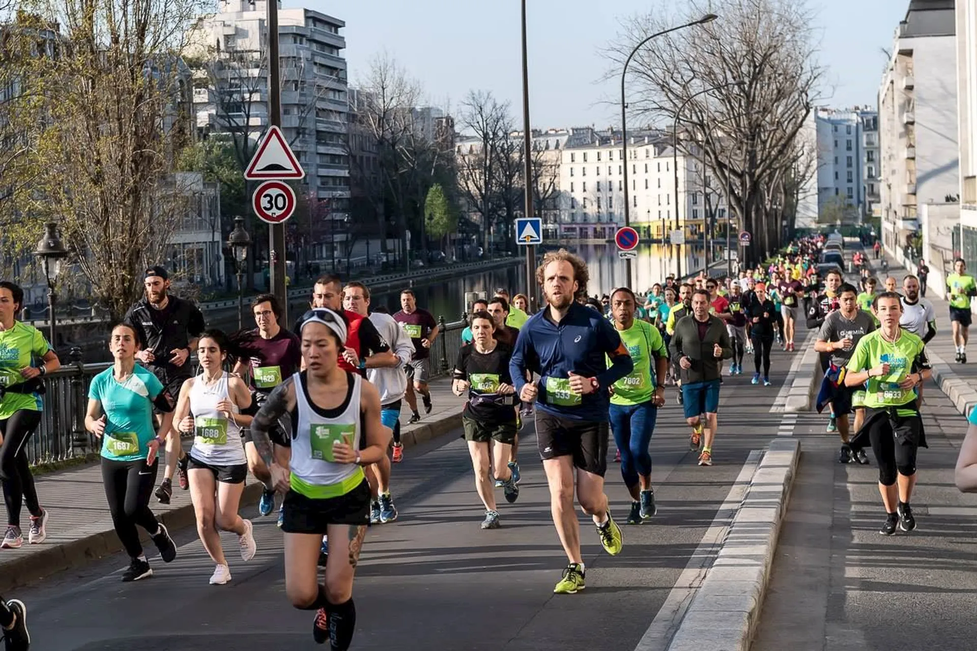 The image depicts a group of runners participating in a road race. The runners are