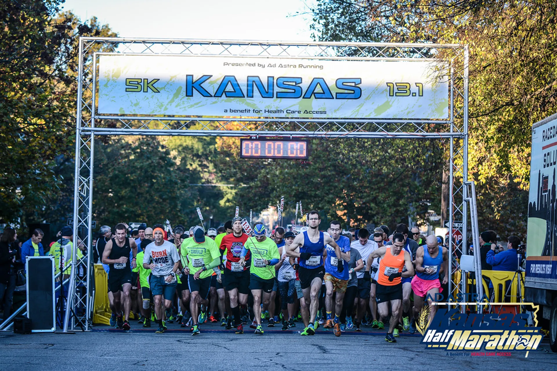 The image shows a group of runners at the starting line of a race. They