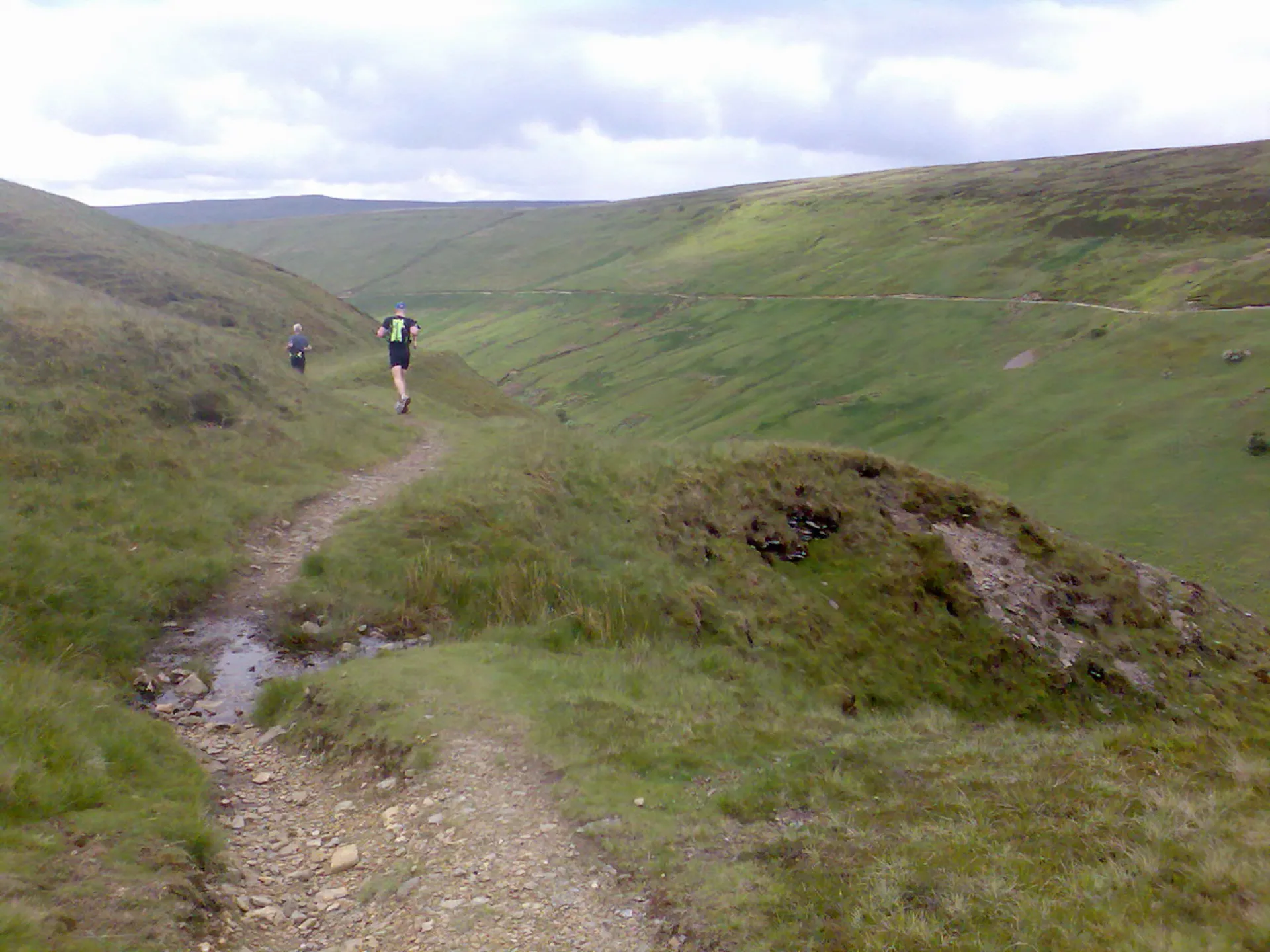 The image shows a scenic landscape with a walking trail. There are two individuals in