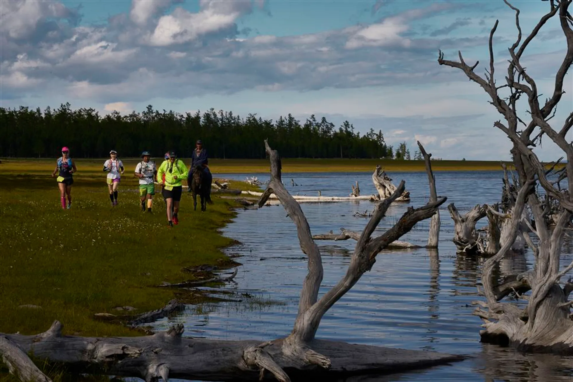 The image features a group of people outdoors in a scenic landscape. They appear to