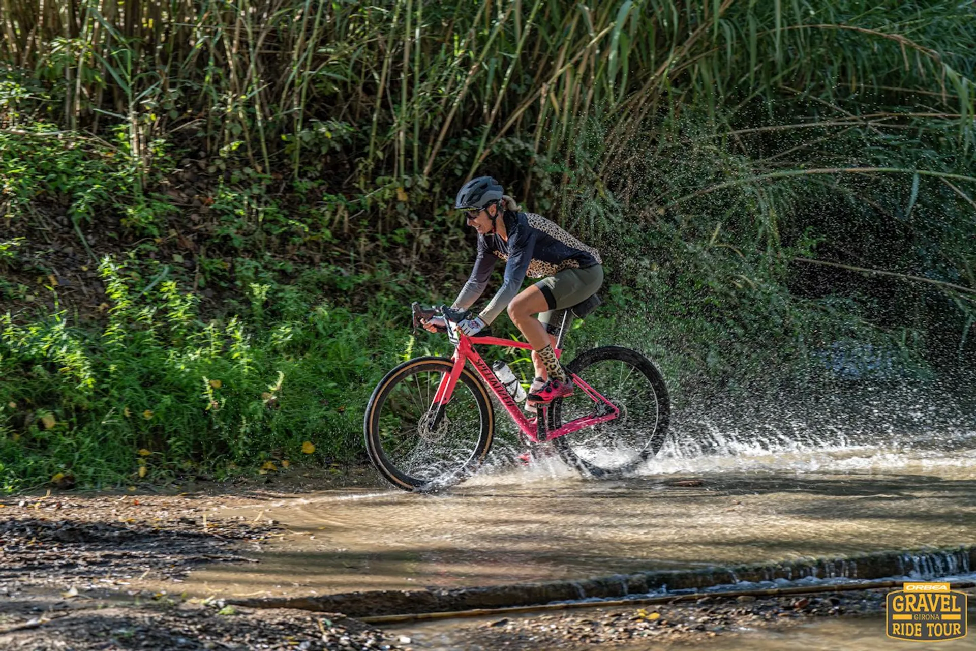 The image shows a person riding a bicycle through a shallow stream or puddle of