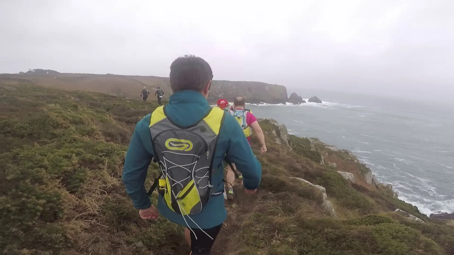 The image shows a group of people hiking along a coastal trail. The person in