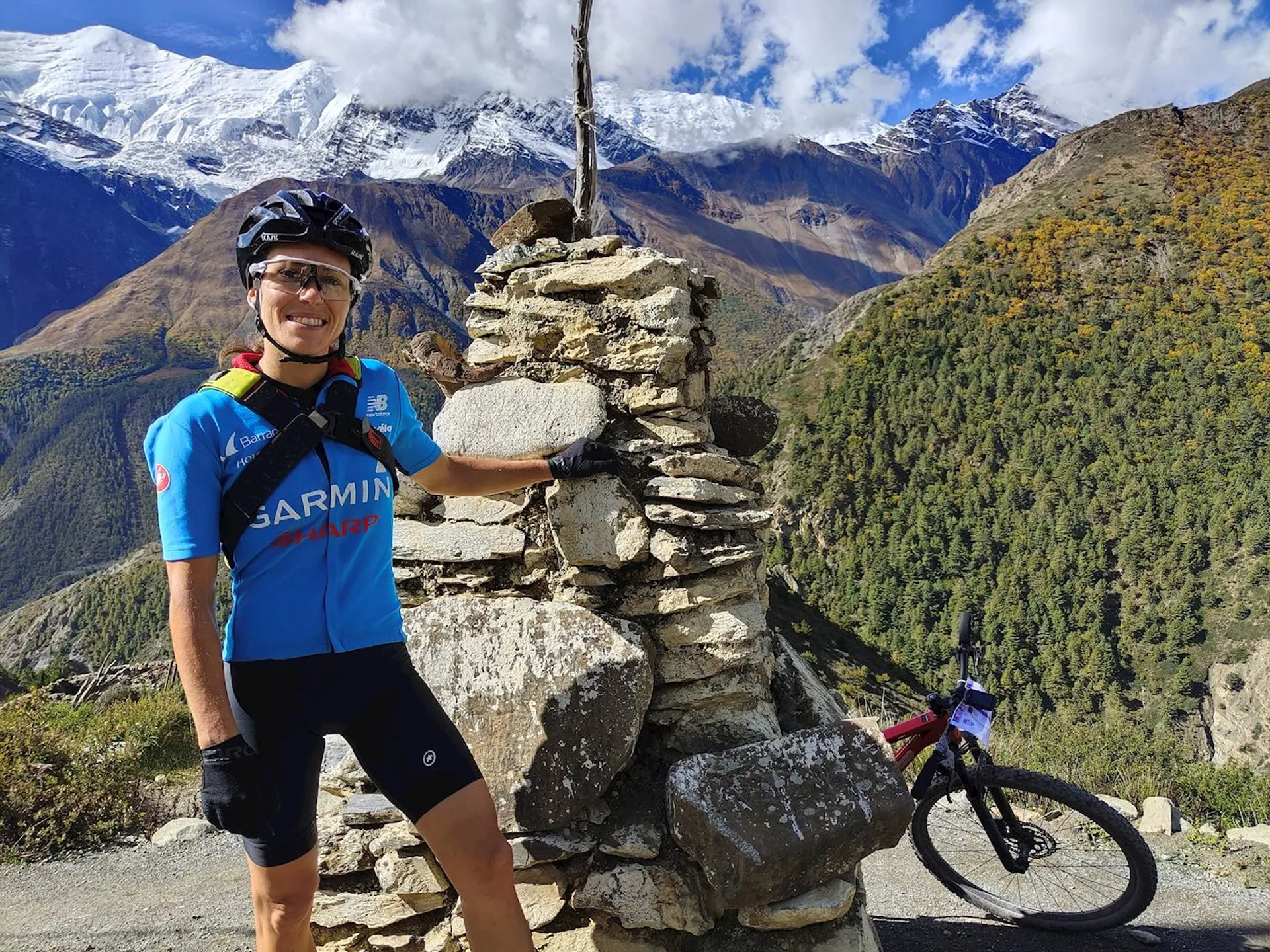 The image shows a person standing next to a stone cairn with a mountain