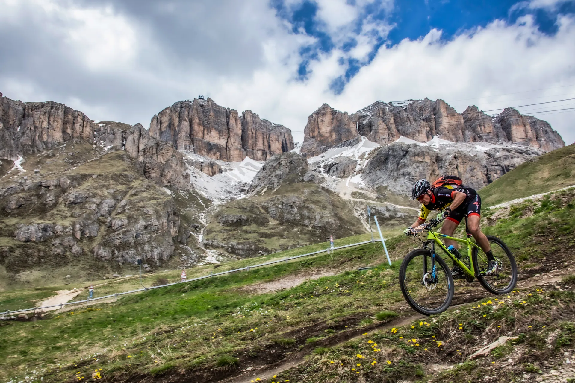 The image shows a mountain biker racing or riding on a grassy trail with