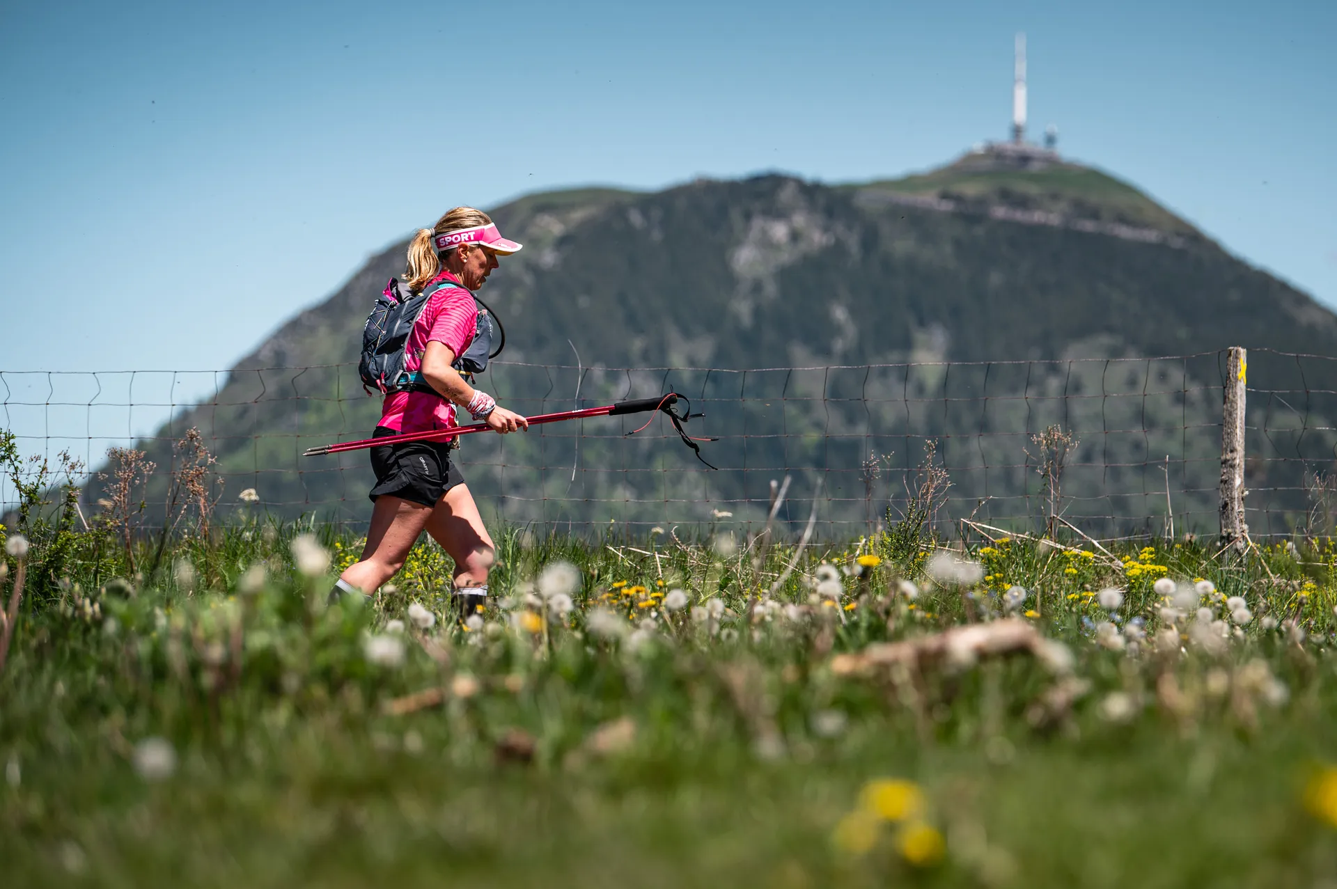 The image depicts a woman hiking in a scenic outdoor environment. She is wearing outdoor