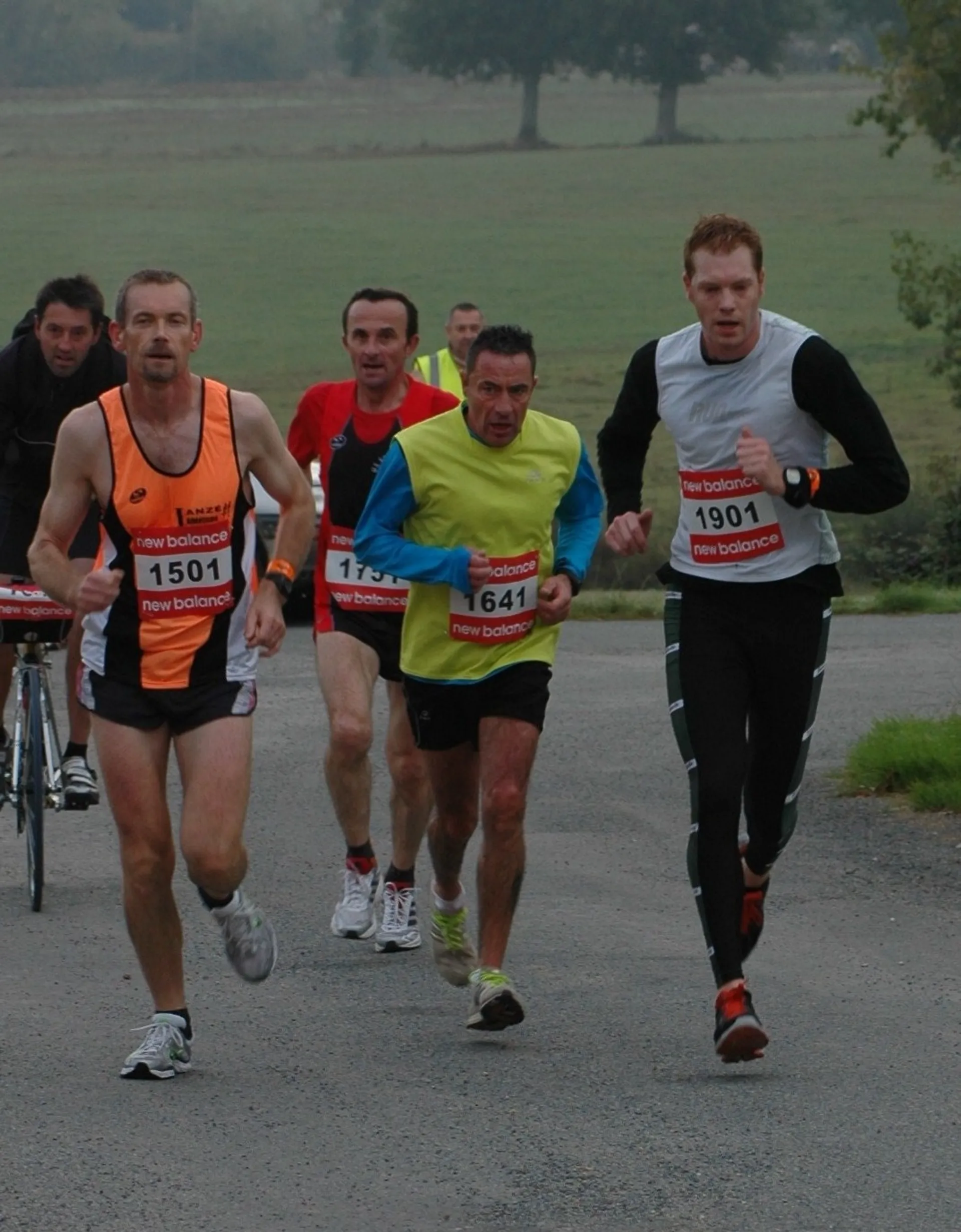 The image shows a group of male runners participating in a road race. They are