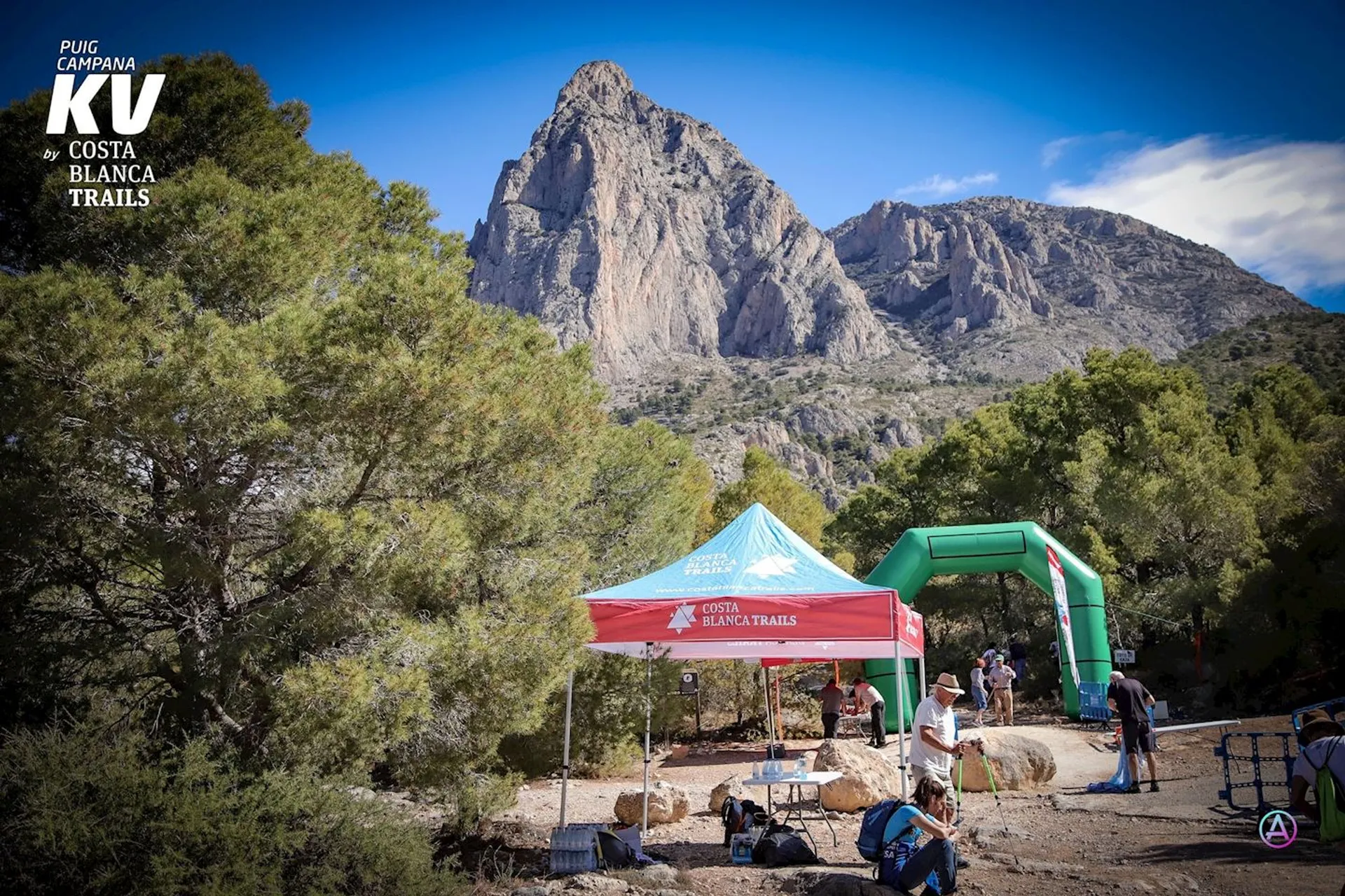 The image shows an outdoor event taking place in a scenic mountainous area under a