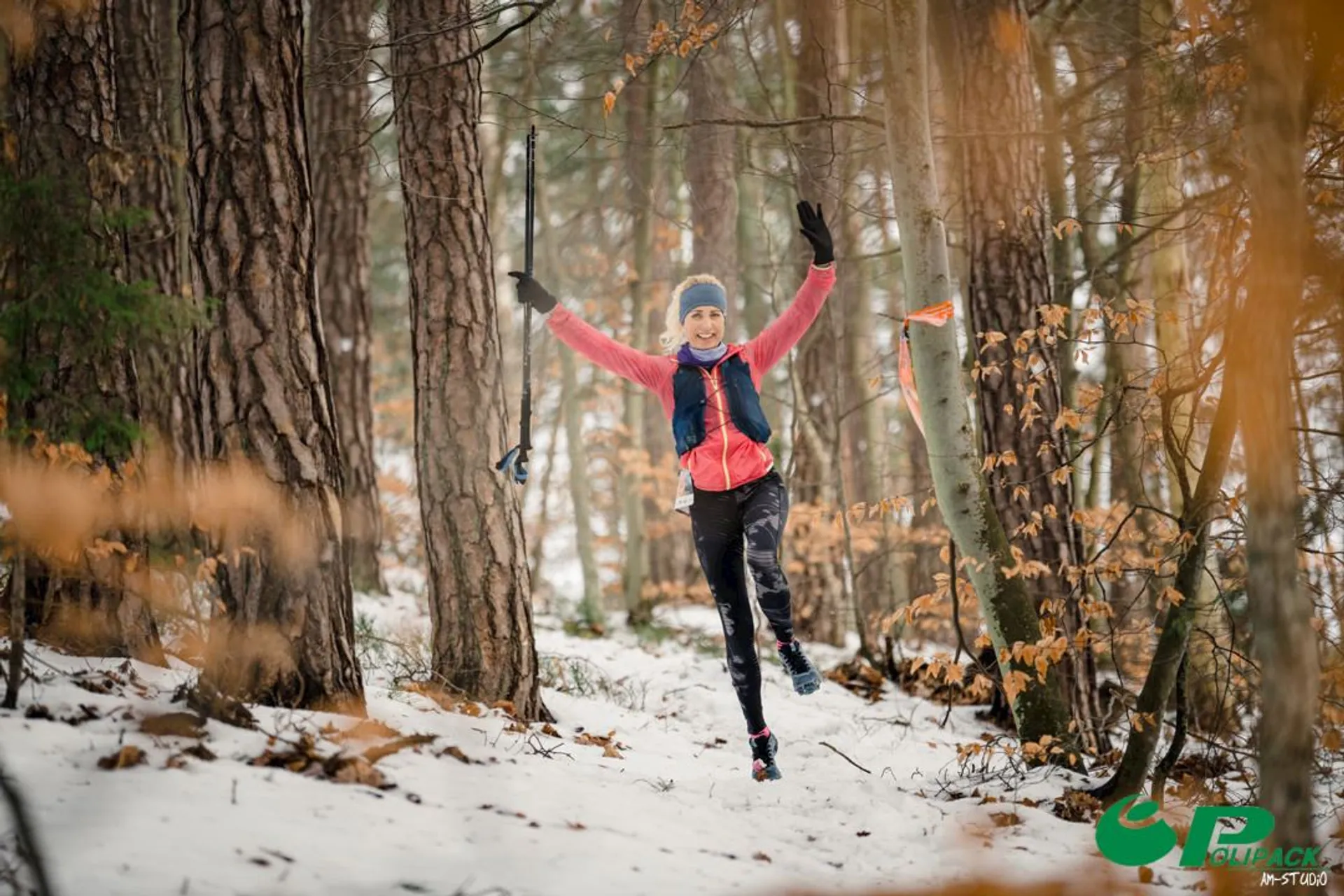 The image shows a person in winter clothing running joyfully through a snowy forest. They look excited with arms raised, surrounded by trees and snow-covered ground. The scene has a vibrant, energetic atmosphere.