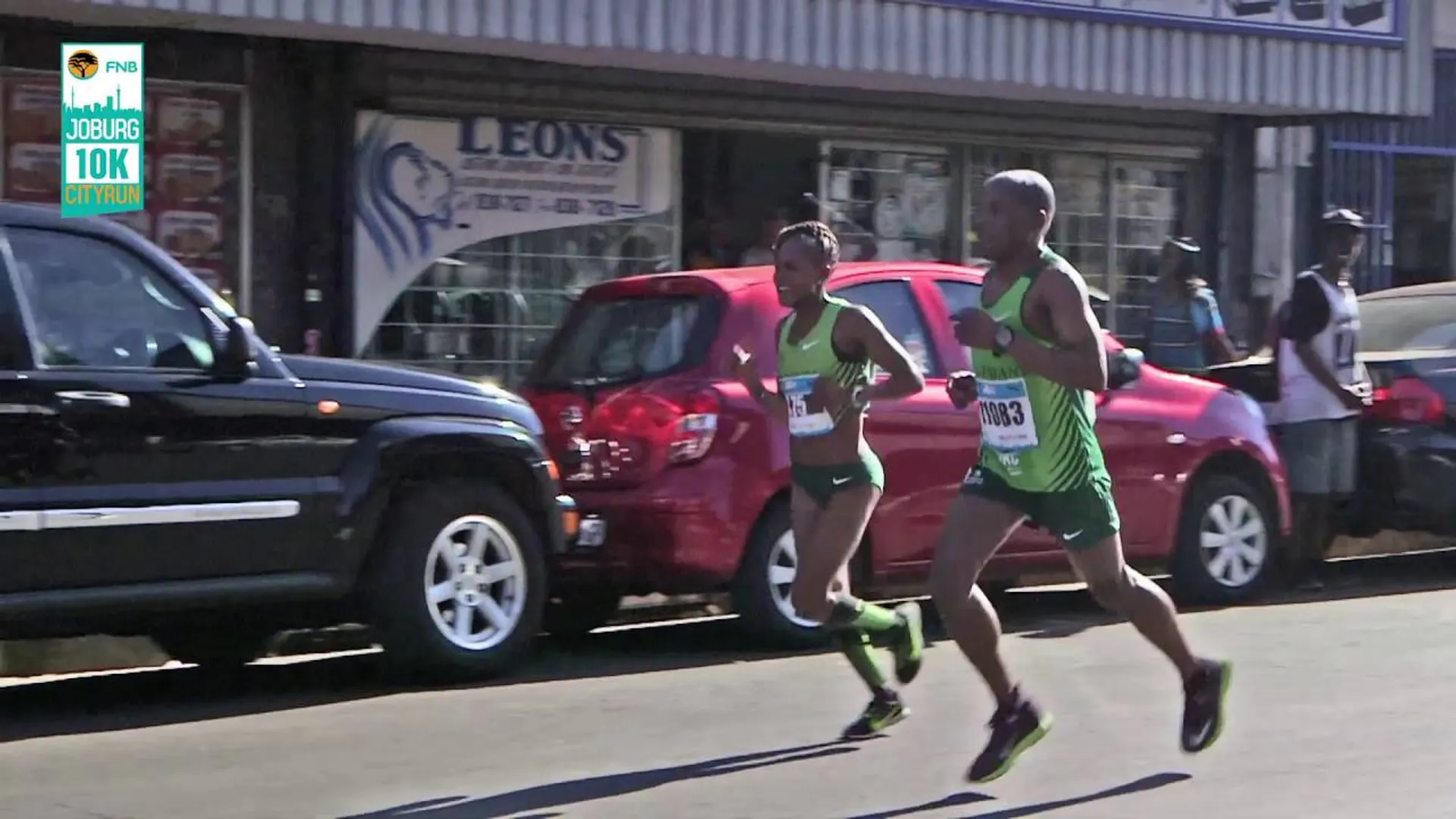 The image shows two athletes running in what appears to be a road race event,