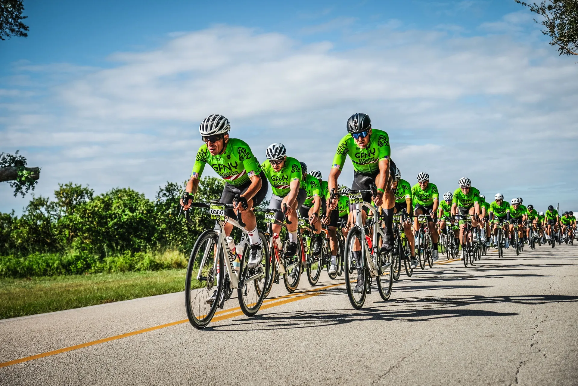 The image depicts a group of cyclists riding on a road, likely participating in a