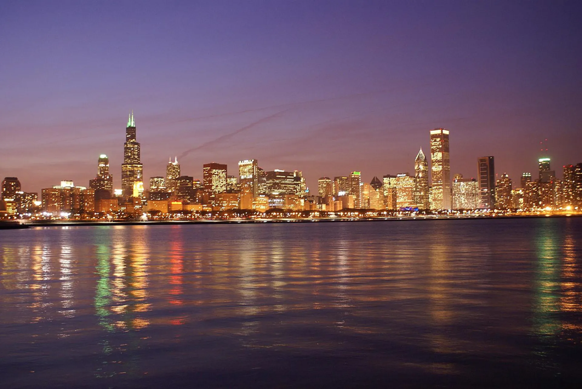 The image displays a city skyline at twilight. The prominent buildings are illuminated, creating