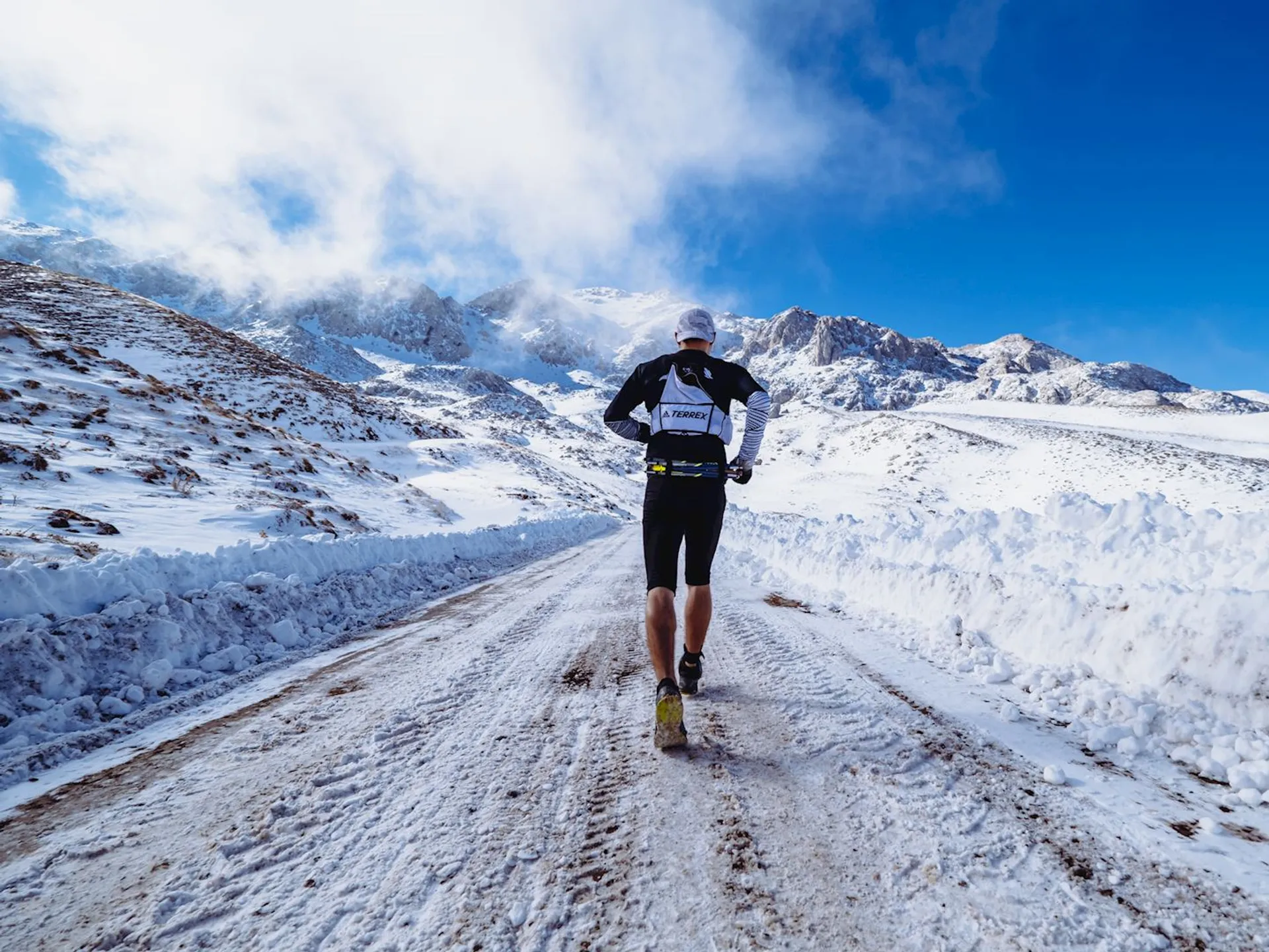 The image shows a person running on a snow-covered road amidst a mountainous landscape