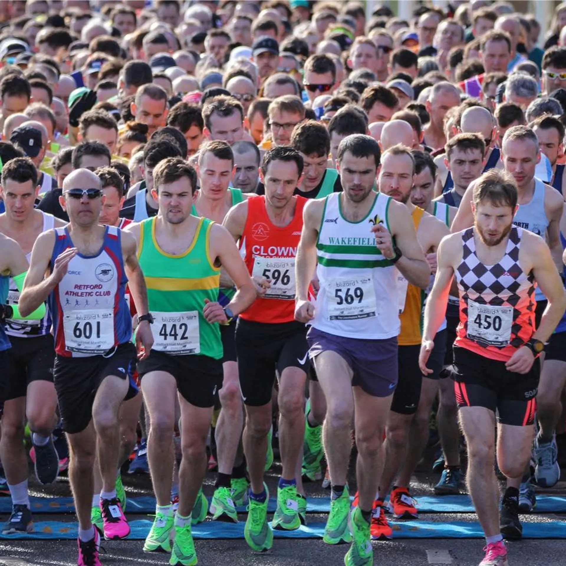 The image shows a group of runners at the starting line of a race. They