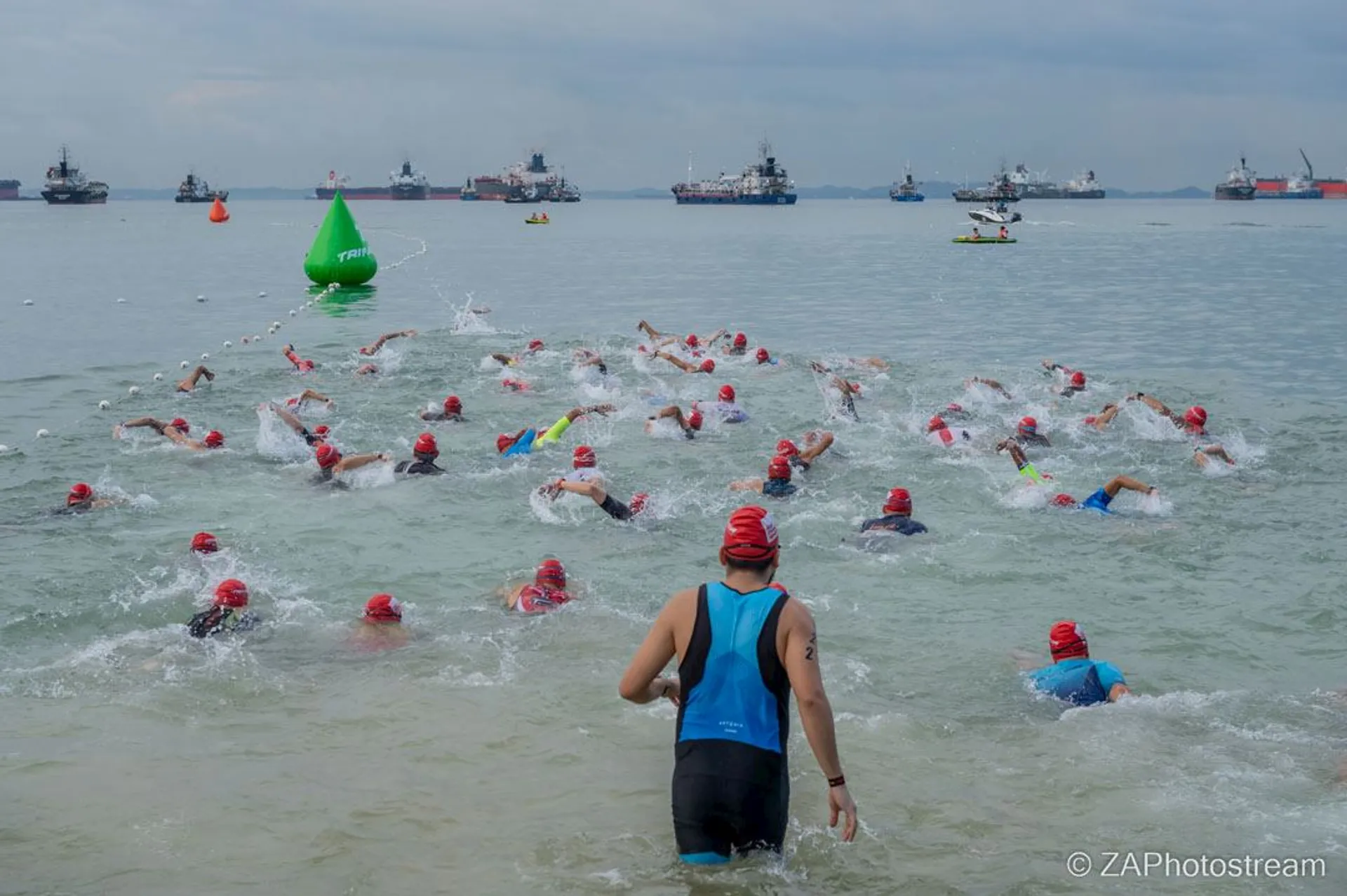 The image shows a group of swimmers in open water, wearing swim caps of