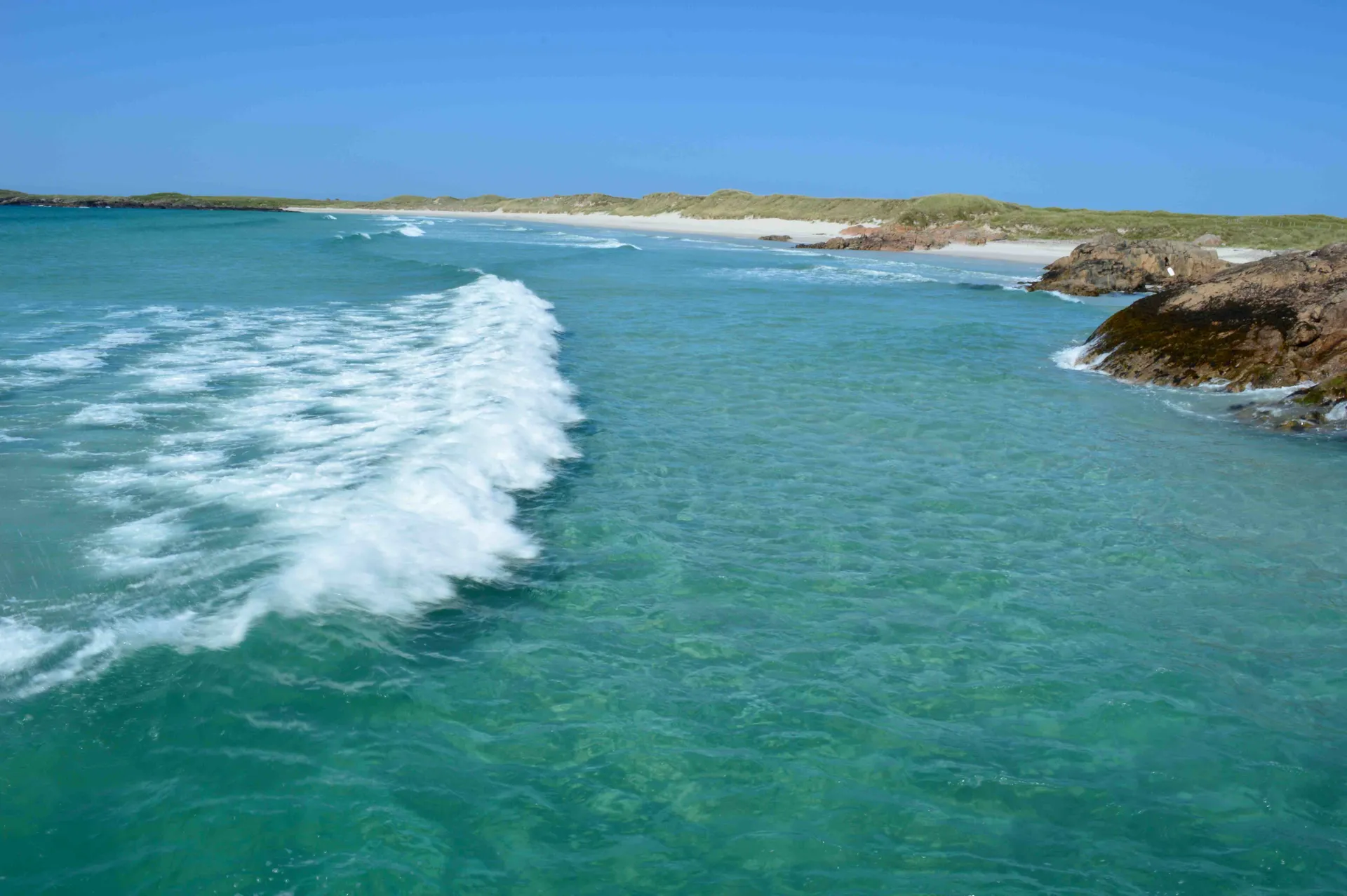 The image shows a beautiful coastal scene featuring clear turquoise water. A wave is breaking