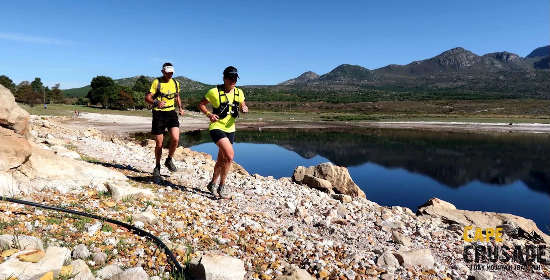The image shows two individuals engaging in trail running adjacent to a body of water,