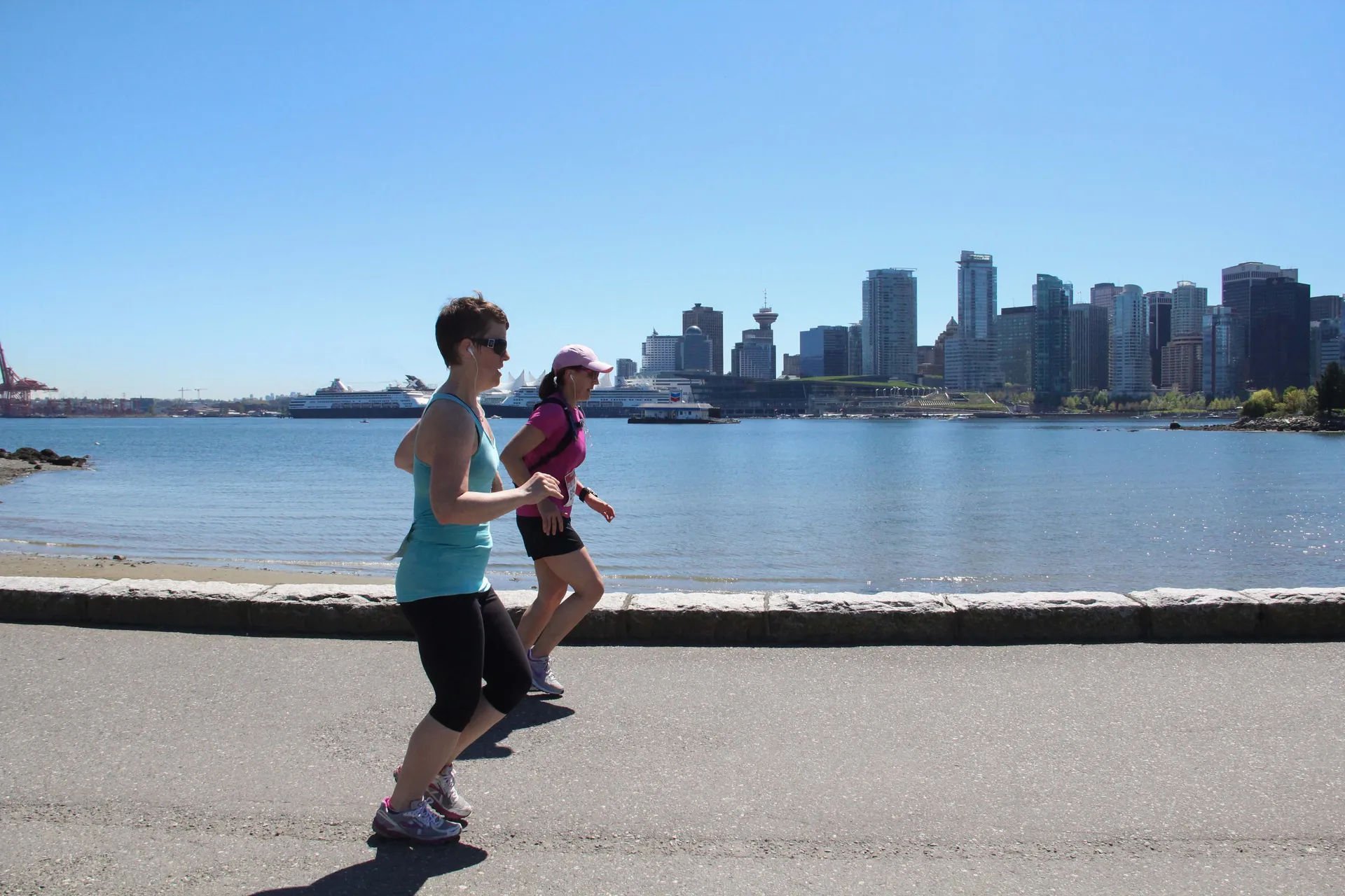 The image shows two individuals jogging along a waterfront path with a city skyline in the