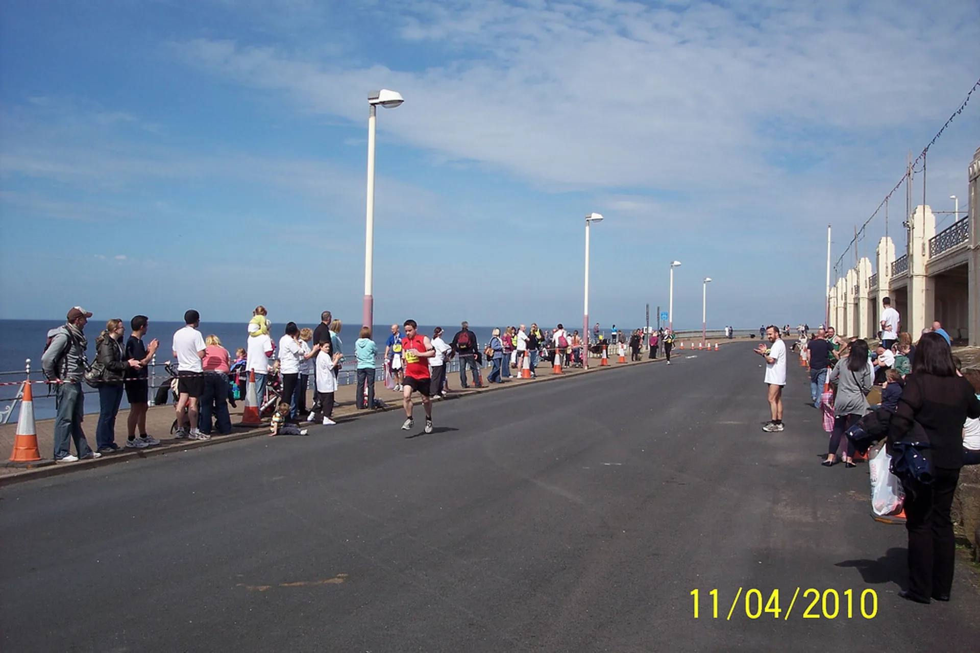 The image depicts a group of people gathered on a wide, open street next to