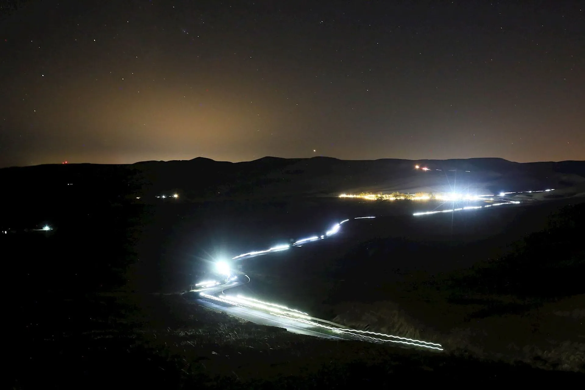 The image depicts a nighttime landscape with a long exposure capturing the light trails of vehicles