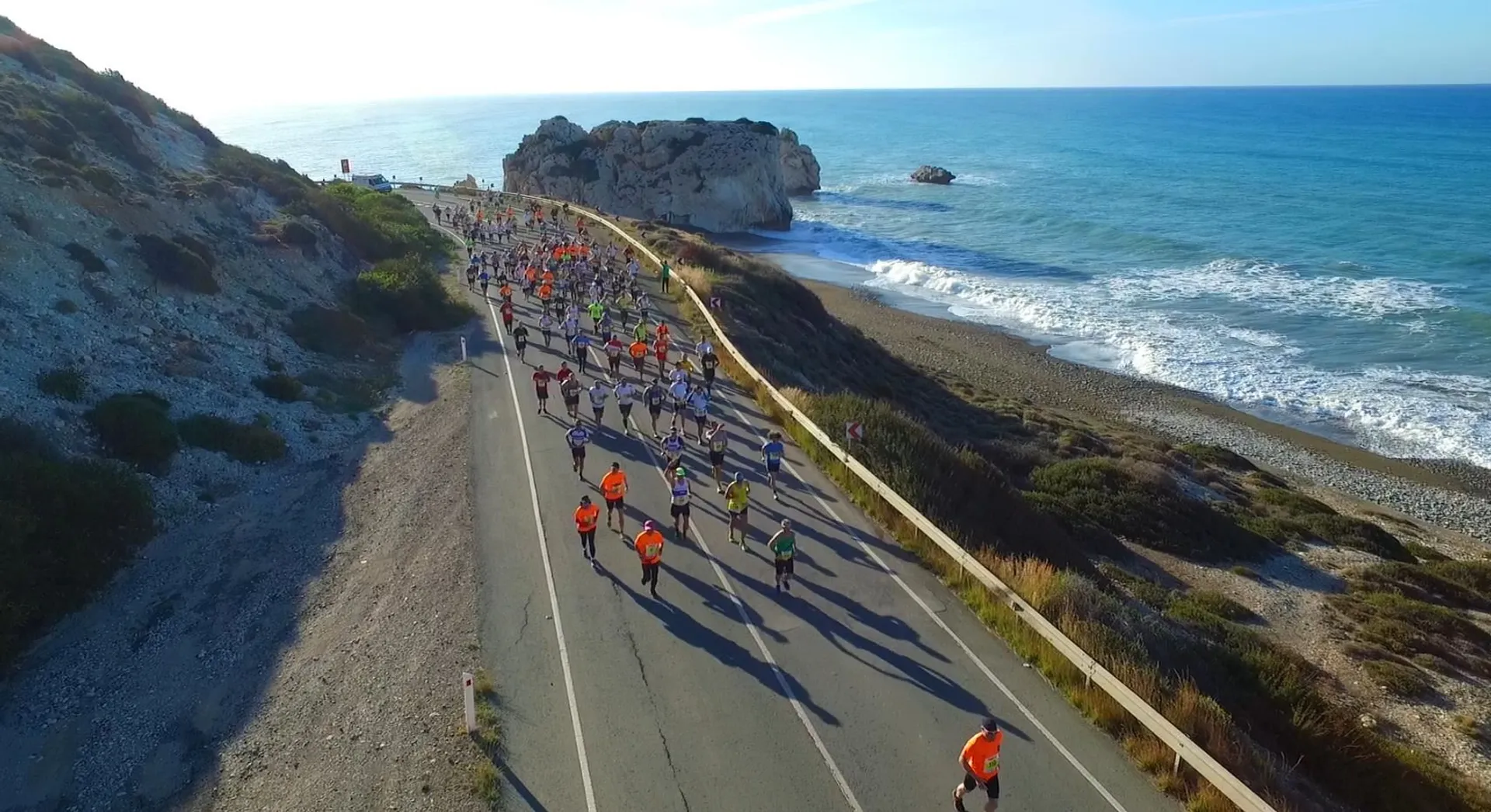 The image shows a scenic coastline with a large group of people participating in a running