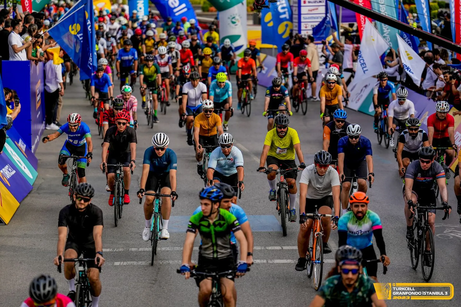 The image shows a large group of cyclists participating in a cycling event. They are