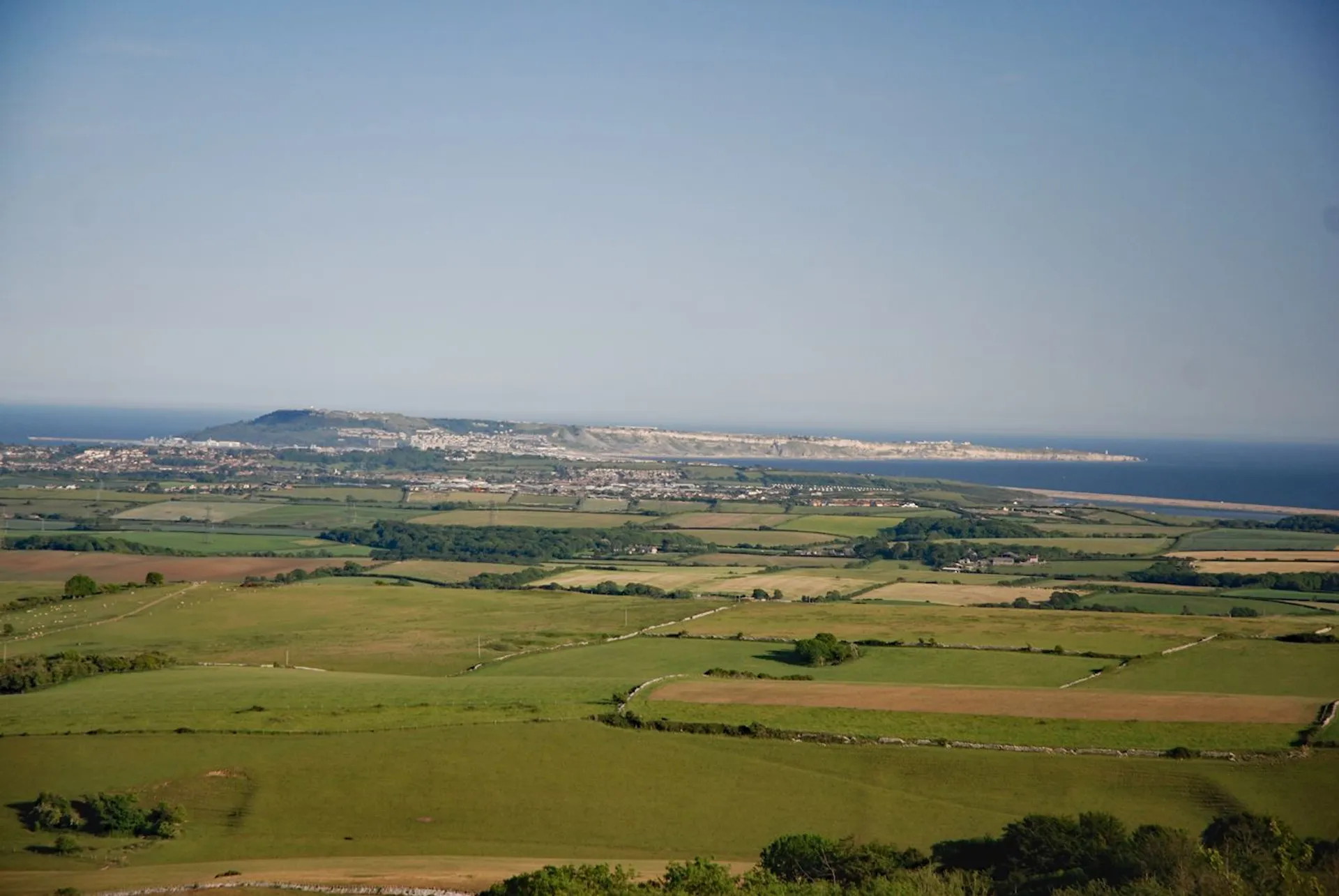 The image shows a sweeping vista of a coastal landscape. It includes expansive green fields