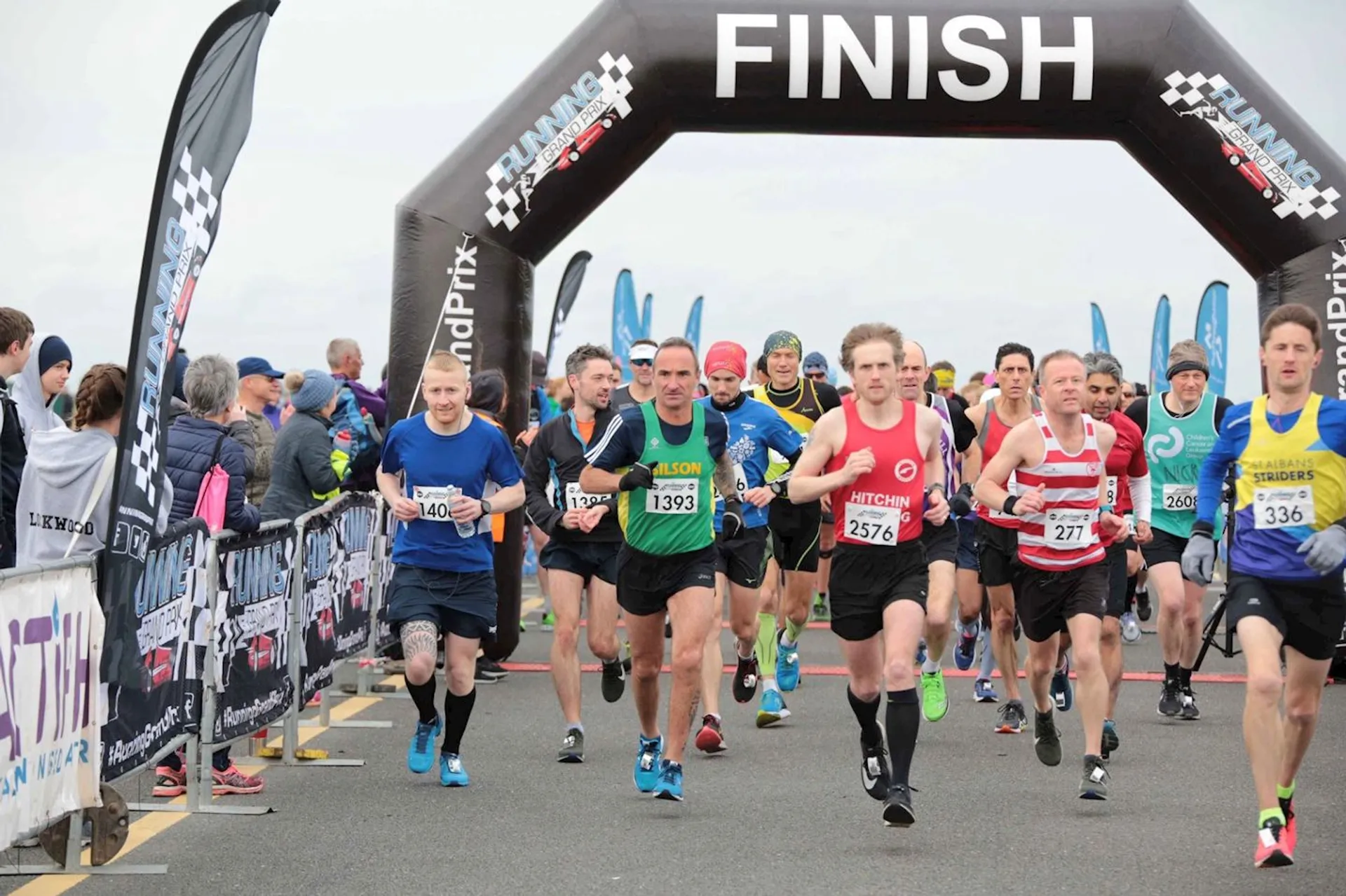 The image shows a group of runners crossing the finish line at a road race event