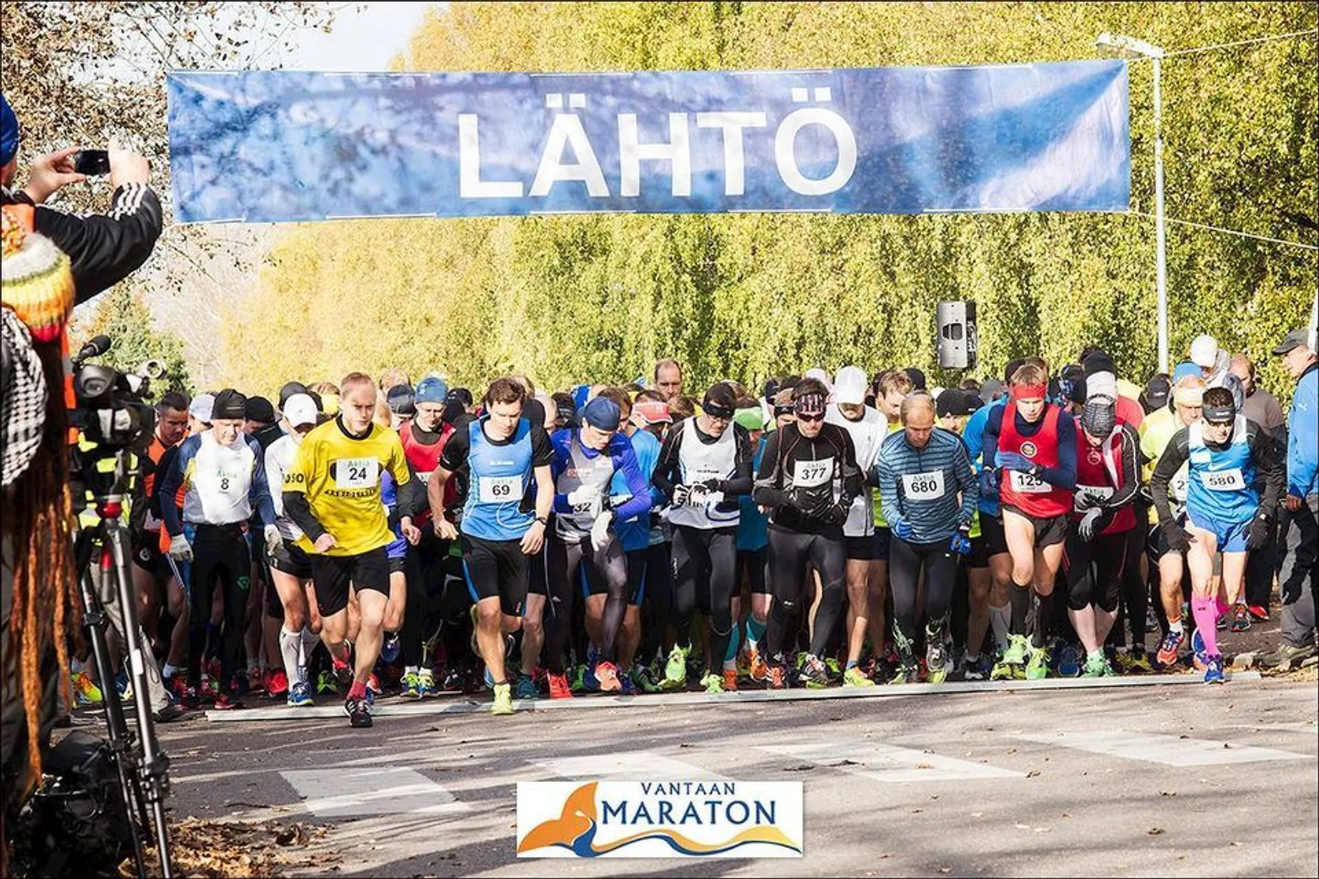 The image shows a group of runners at the start line of a marathon. They