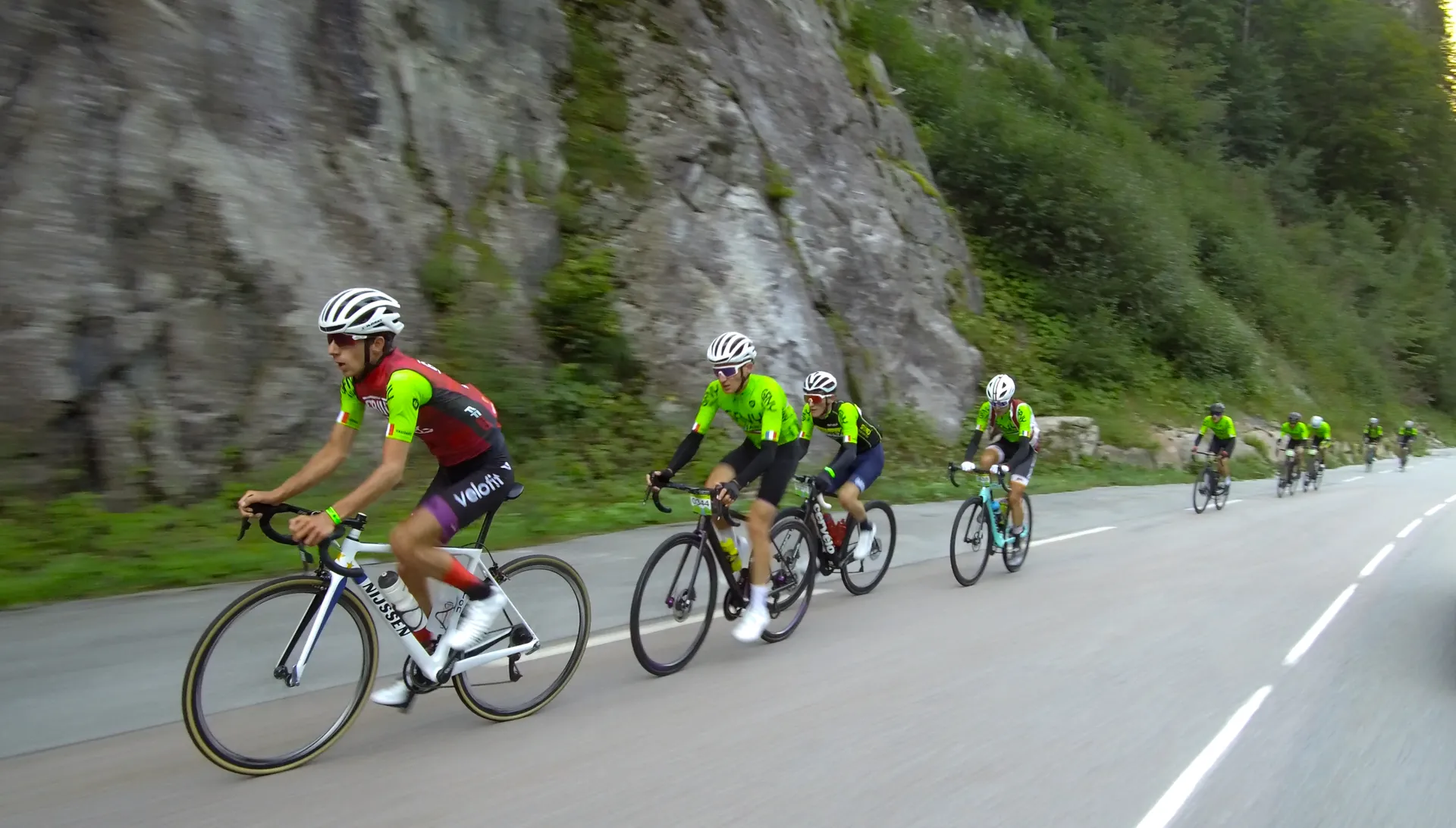 The image depicts a group of cyclists riding on a road. The cyclists are wearing