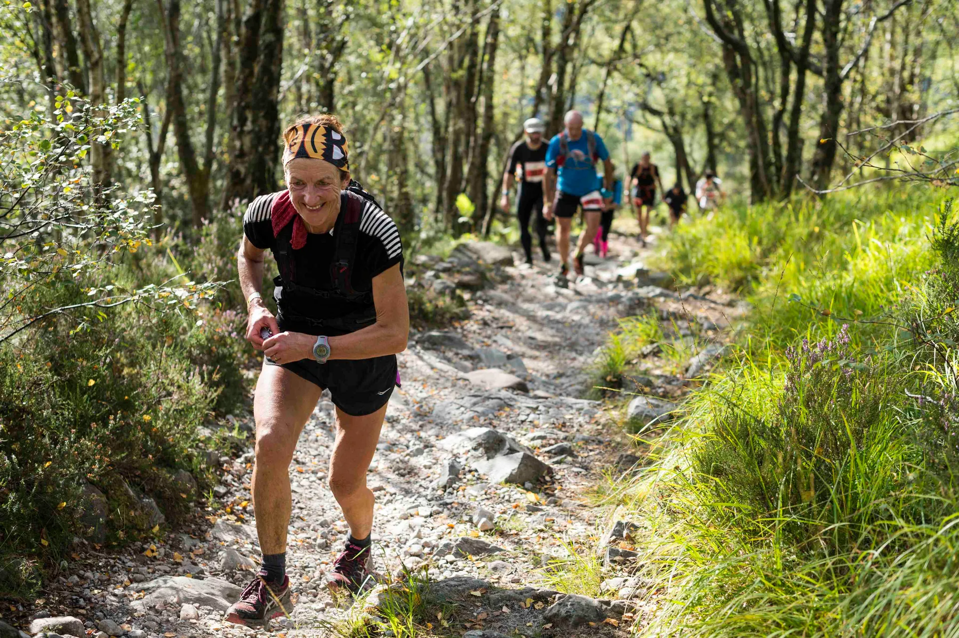 The image shows a group of individuals participating in a trail running event. The foreground