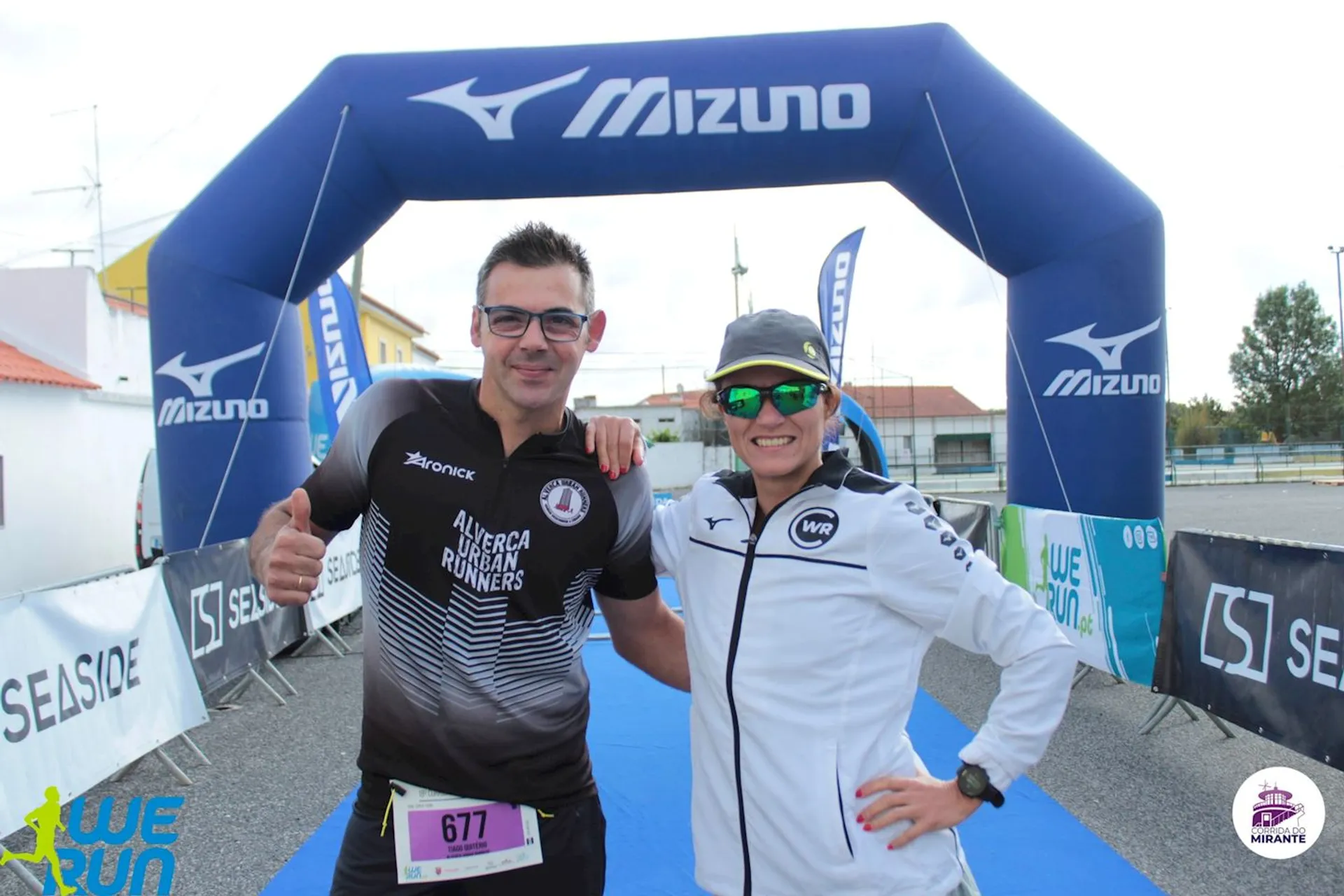 The image shows two people posing together under an inflatable arch with the Mizuno logo
