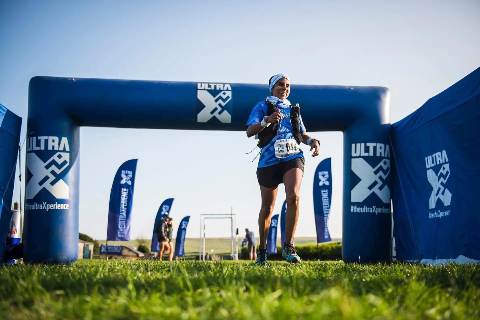The image shows a runner crossing the finish line of a race. The runner is