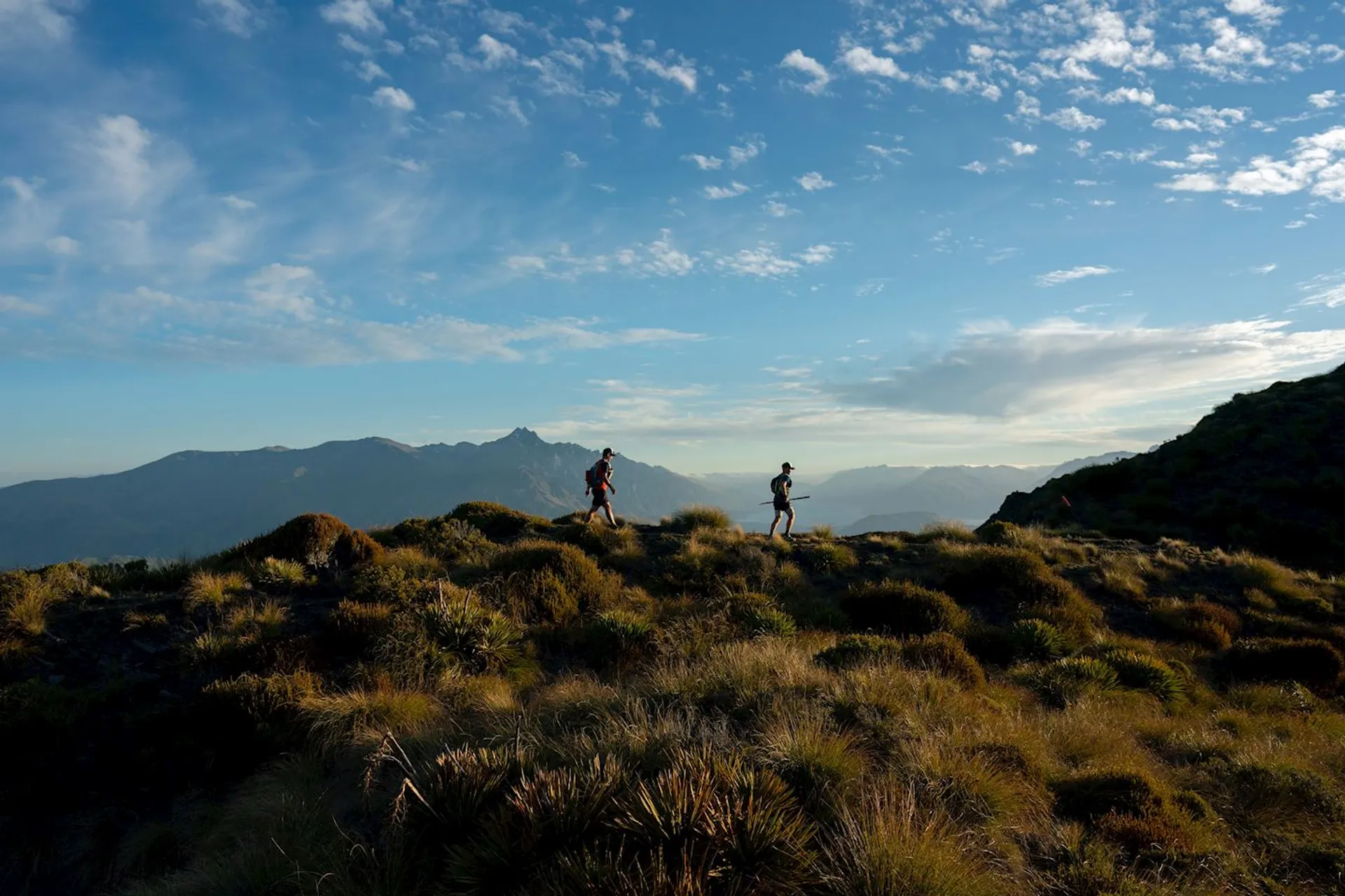 This image depicts two hikers with backpacks traversing across a mountainous landscape