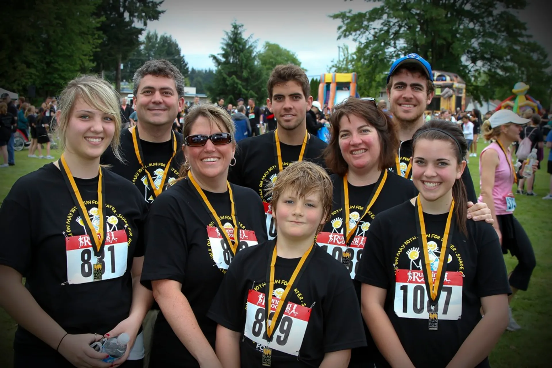 The image depicts a group of seven people posing together outdoors. They appear to be