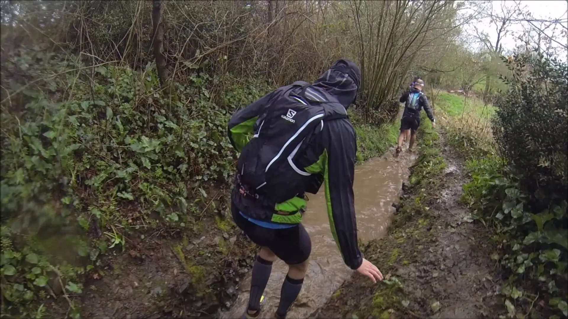 The image shows a group of people engaged in trail running or hiking through a muddy