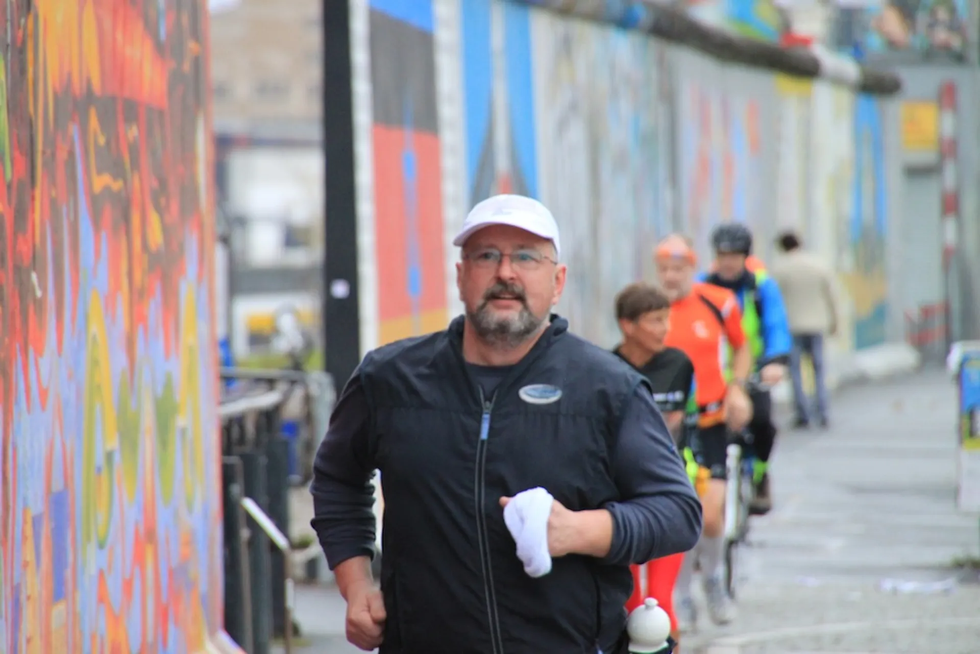 The image shows a man jogging toward the camera, holding what appears to be a